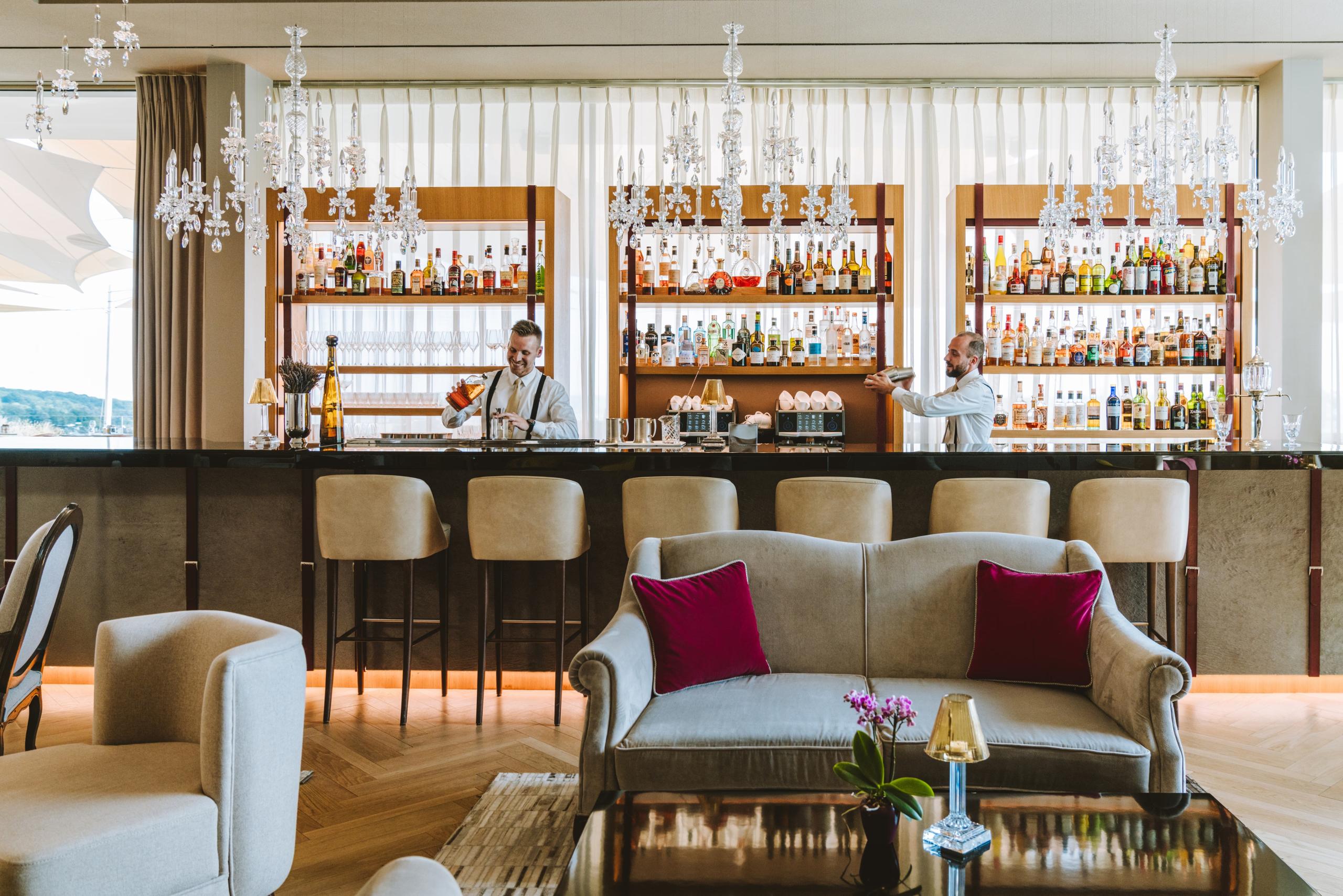 Modern bar with extensive shelving, wine bottles displayed, and upholstered bar seating