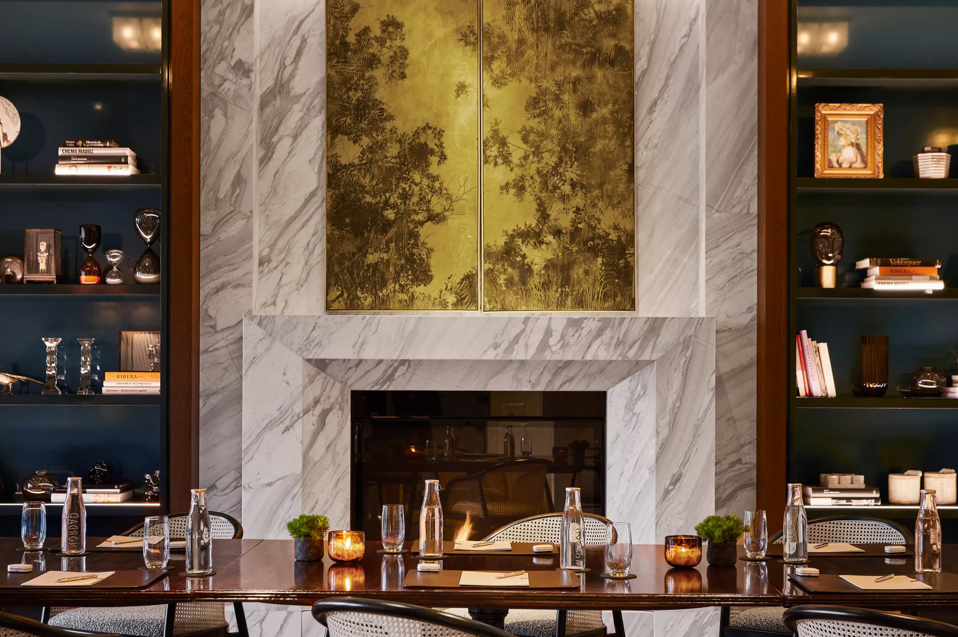 A fireplace with marble surround, gold leaf artwork, and built-in shelving with decor