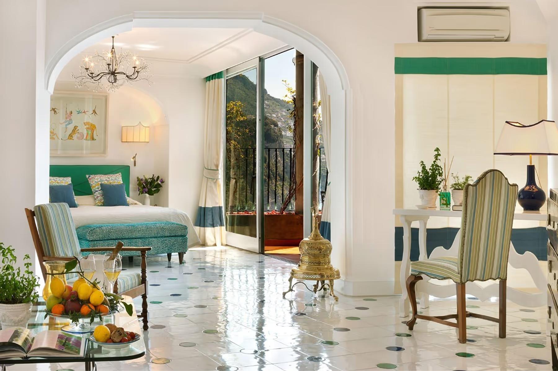 Il San Pietro di Positano: airy bedroom suite with arched entryway, green velvet seating, marble inlay flooring, and open doors to sea terrace