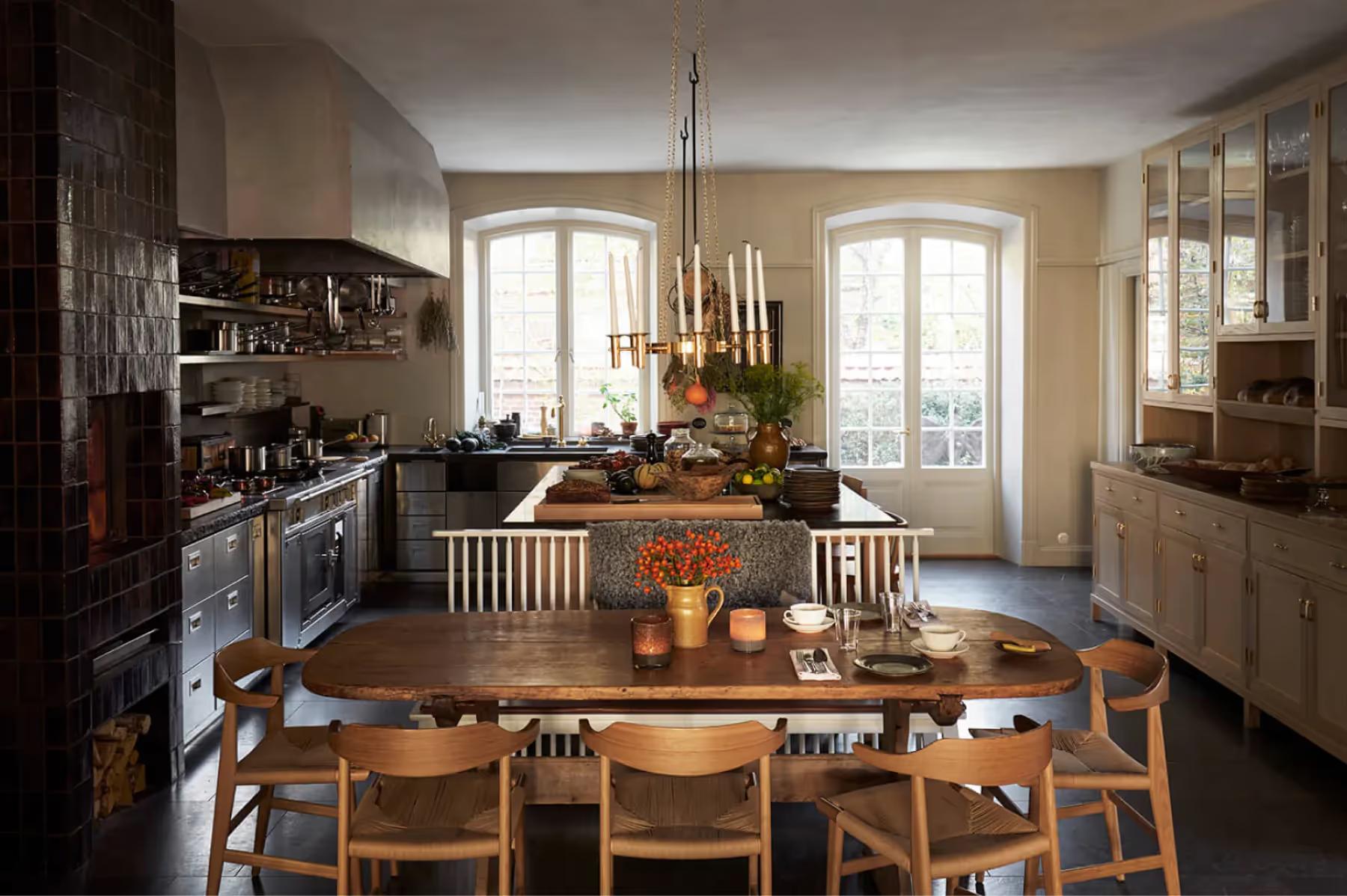 Ett Hem: a kitchen dining room with wooden table, leather chairs, open shelving, and two tall arched windows