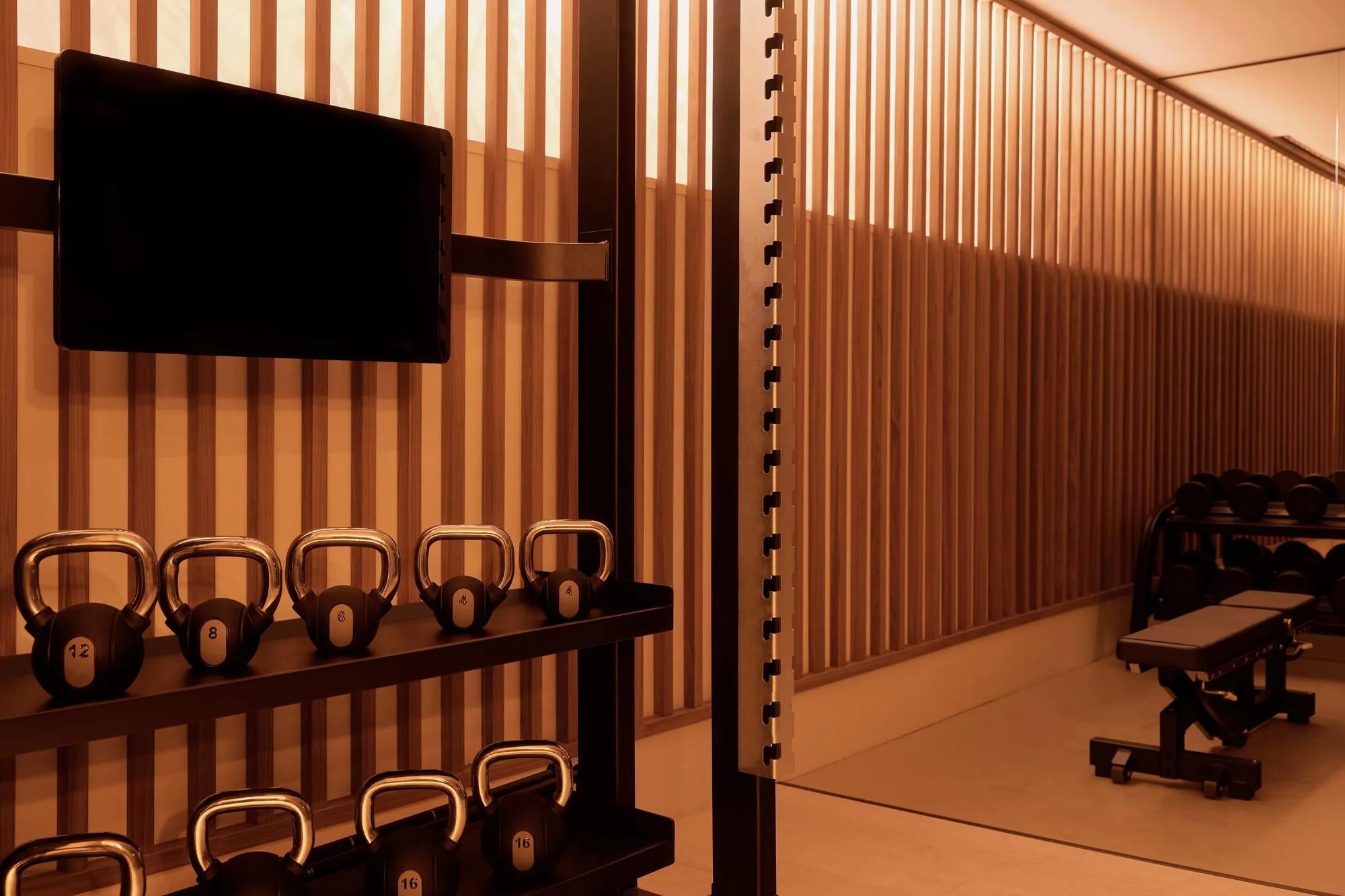 Rosewood Amsterdam: the fitness center with kettlebells, a weight bench, and slatted wood walls