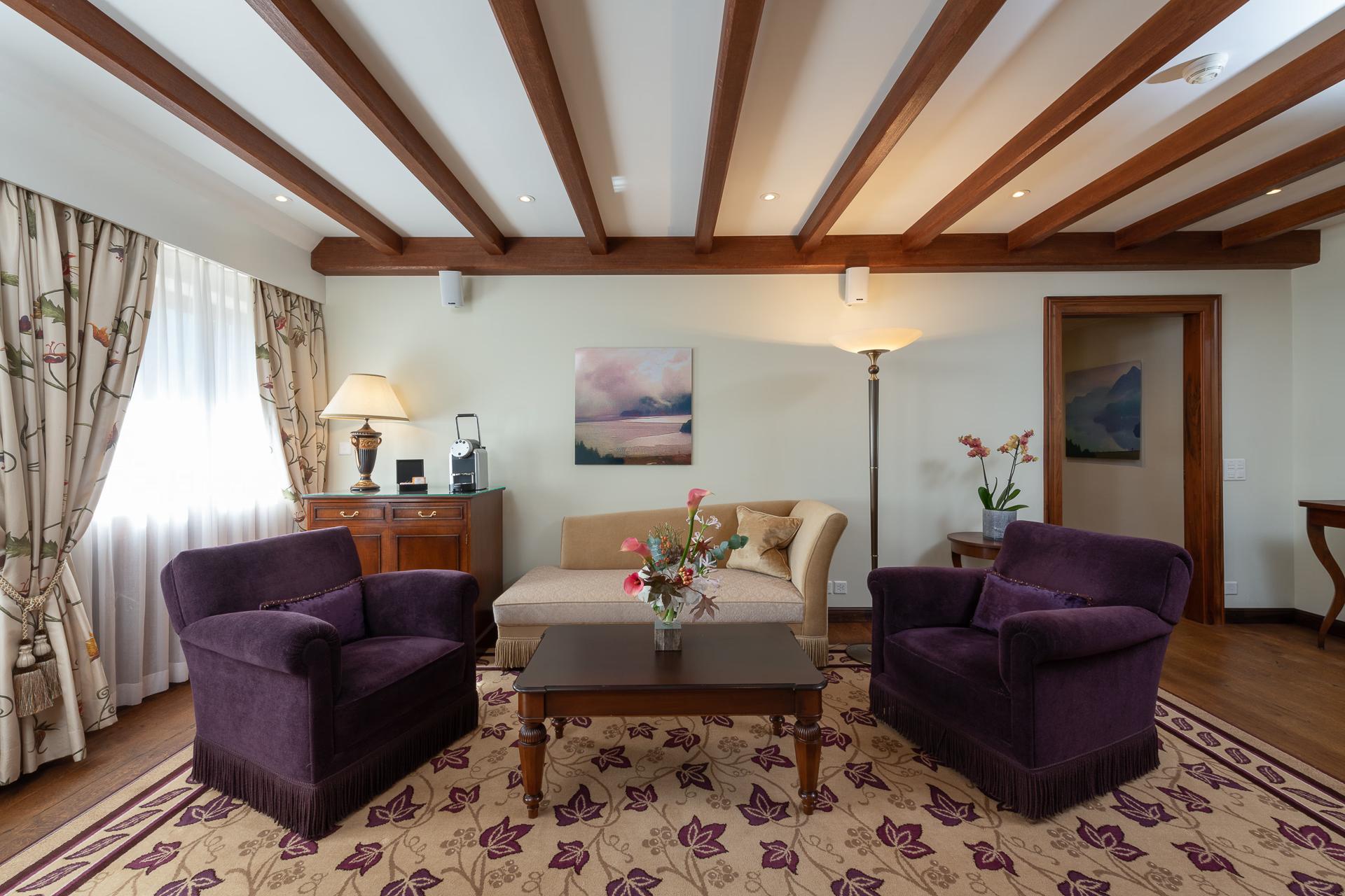 Suvretta House: a suite lounge with exposed timber framing, purple seating, artwork, and soft pendant lighting