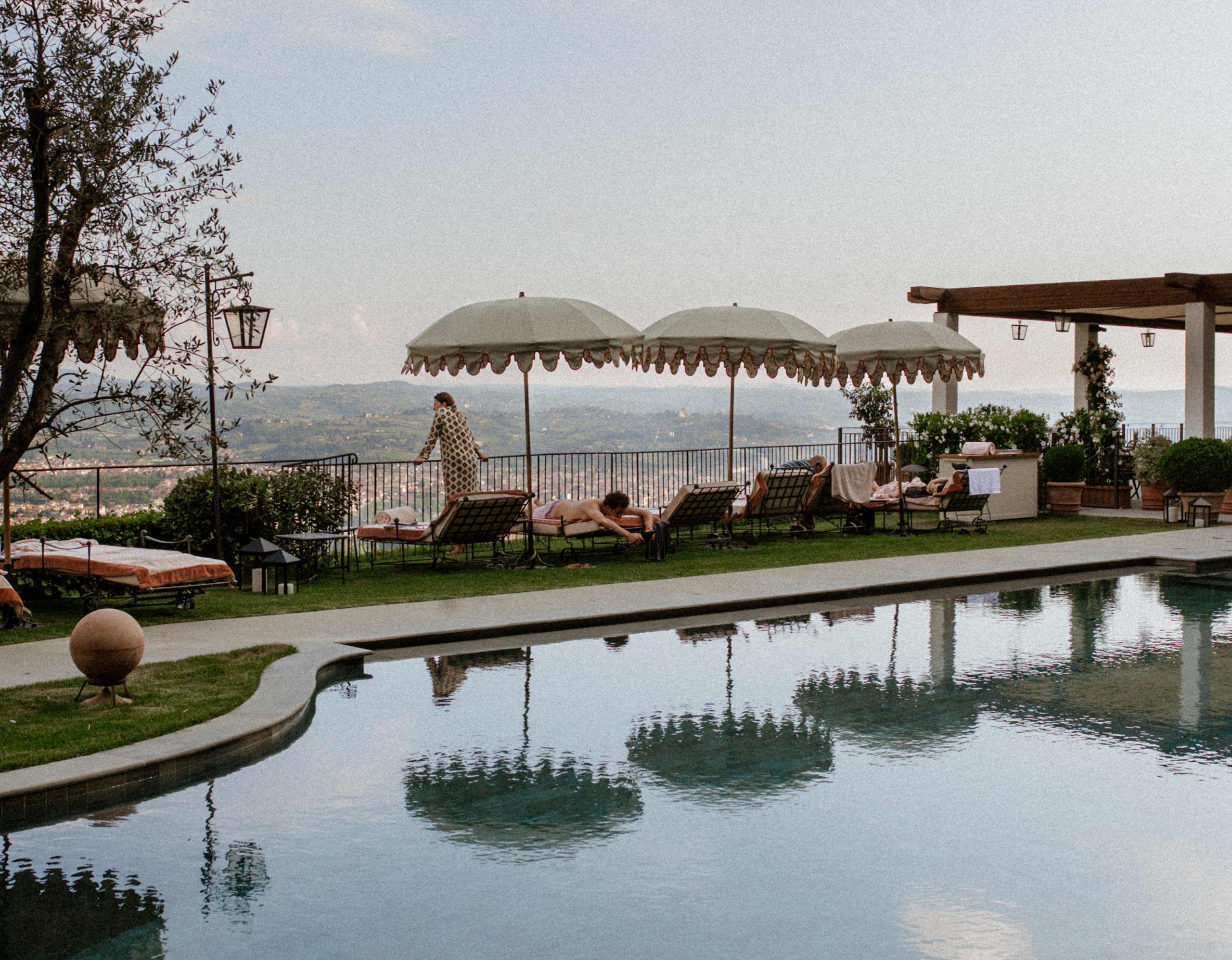 A swimming pool with cypress alleys, terrace seating, and Tuscan valley views beyond