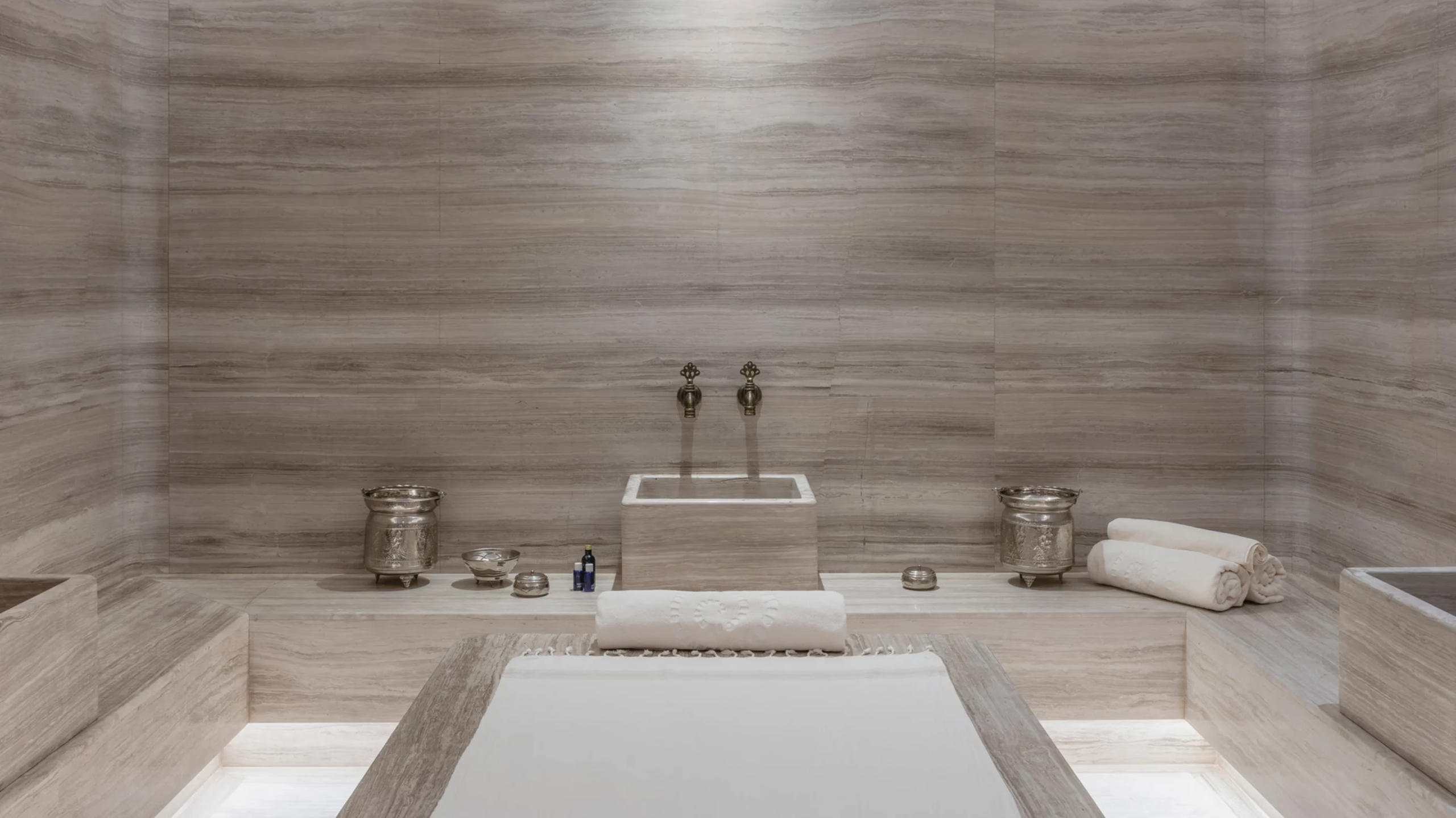 A spa treatment room with rectangular sunken tub and minimal stone finishes