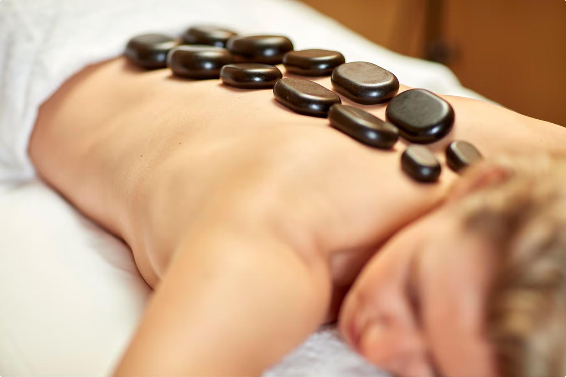 Hot stone therapy treatment being applied to client’s back with therapist’s hands