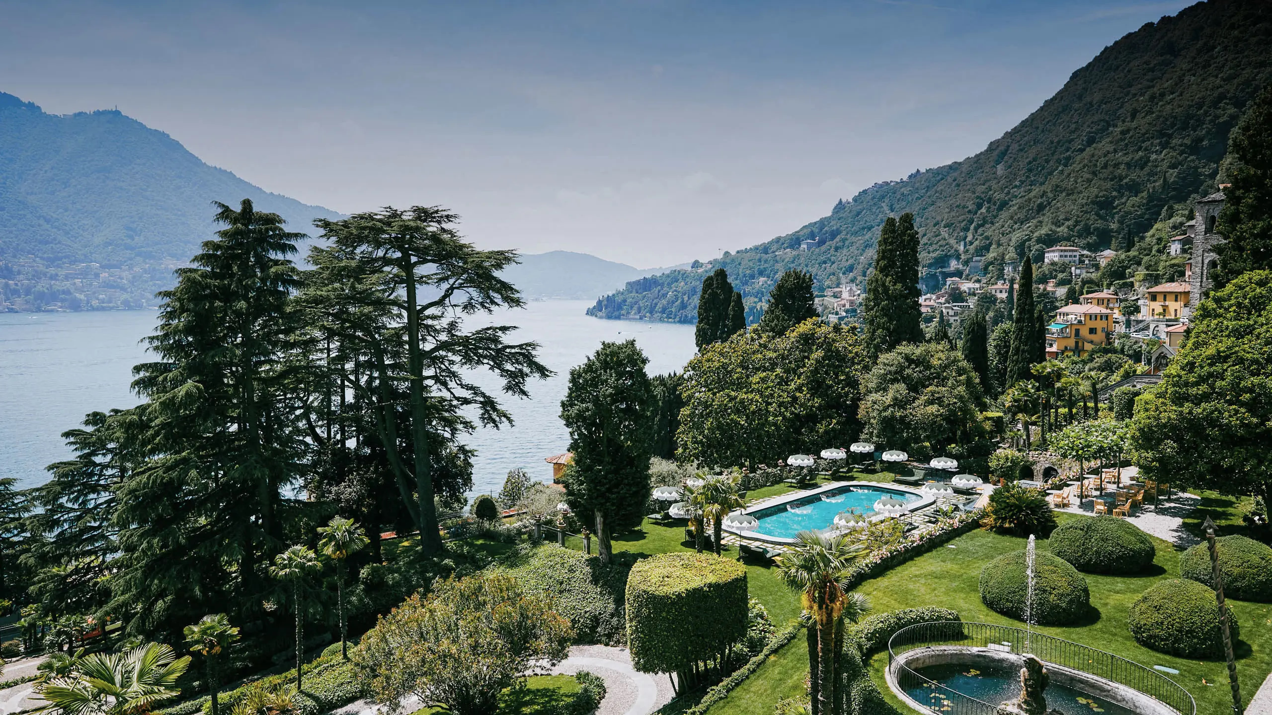Passalacqua: property grounds with pool, cypress trees, lake, and mountains visible beyond
