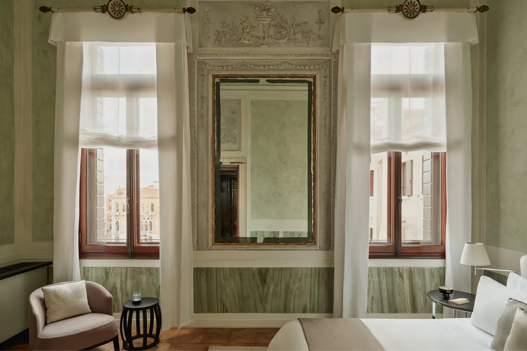Aman Venice: a light-filled room with pale green walls, arched windows, dark-framed mirrors, and cream drapery