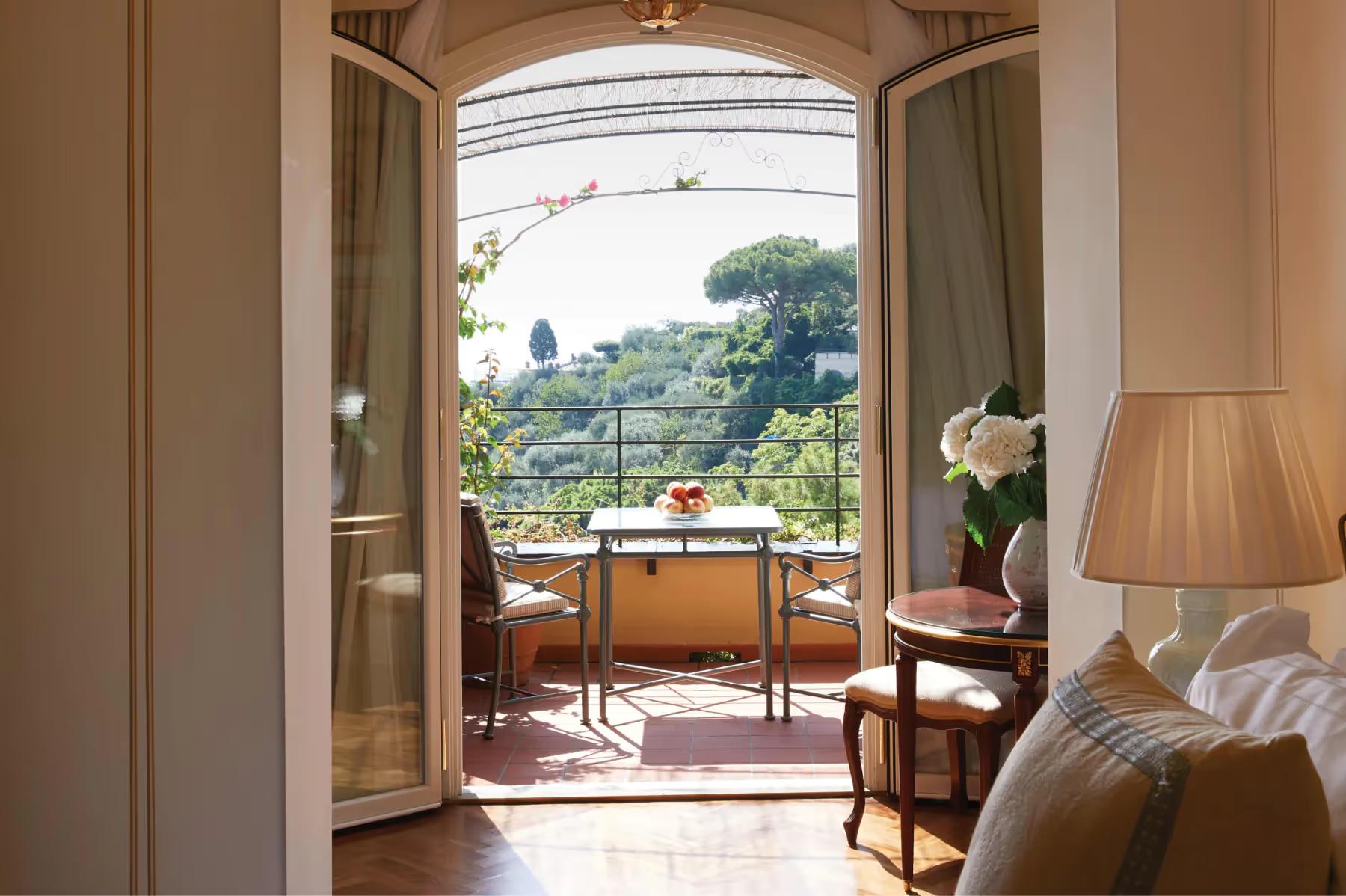 Splendido: a suite living room with upholstered chair and ocean view from open glass doors