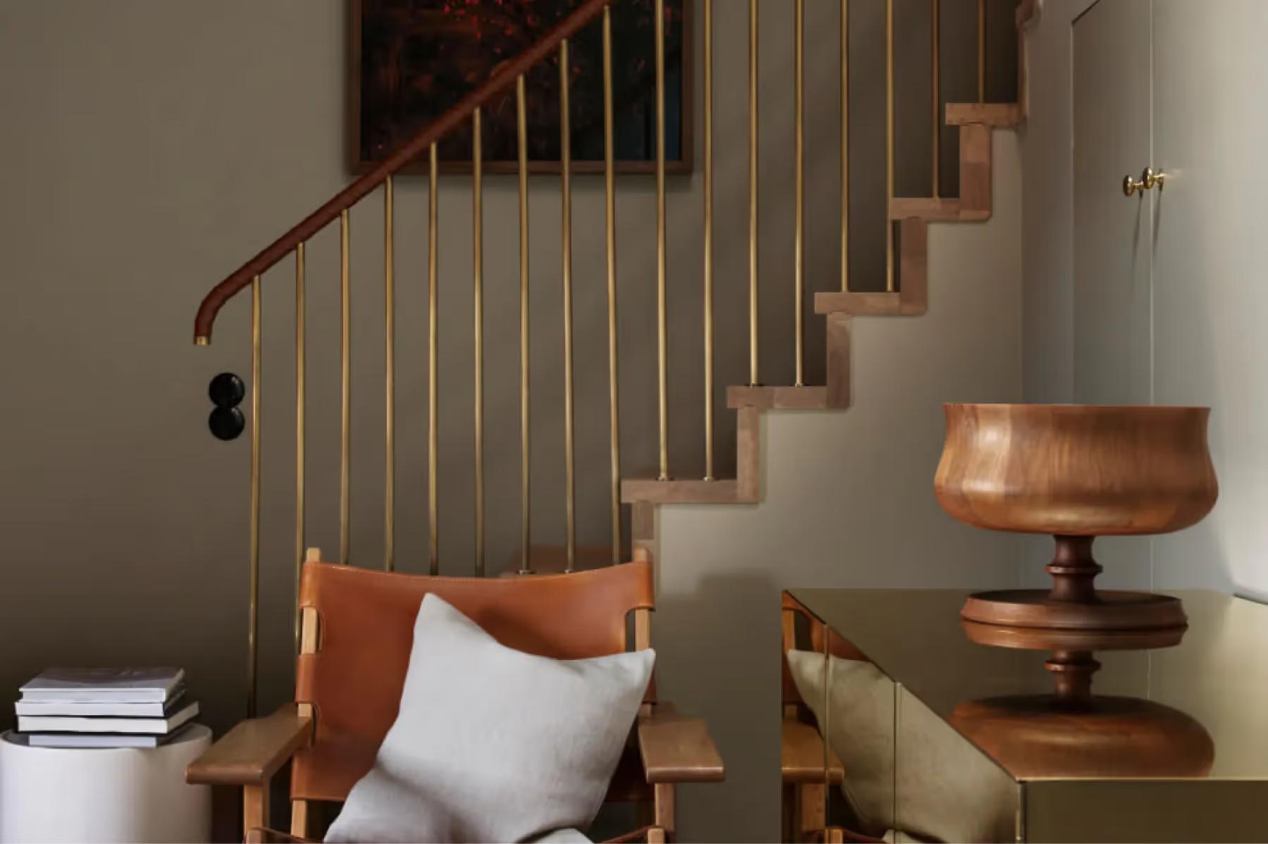 Ett Hem: a timber staircase with metal railing next to a bench with cushions and a side table with stacked books