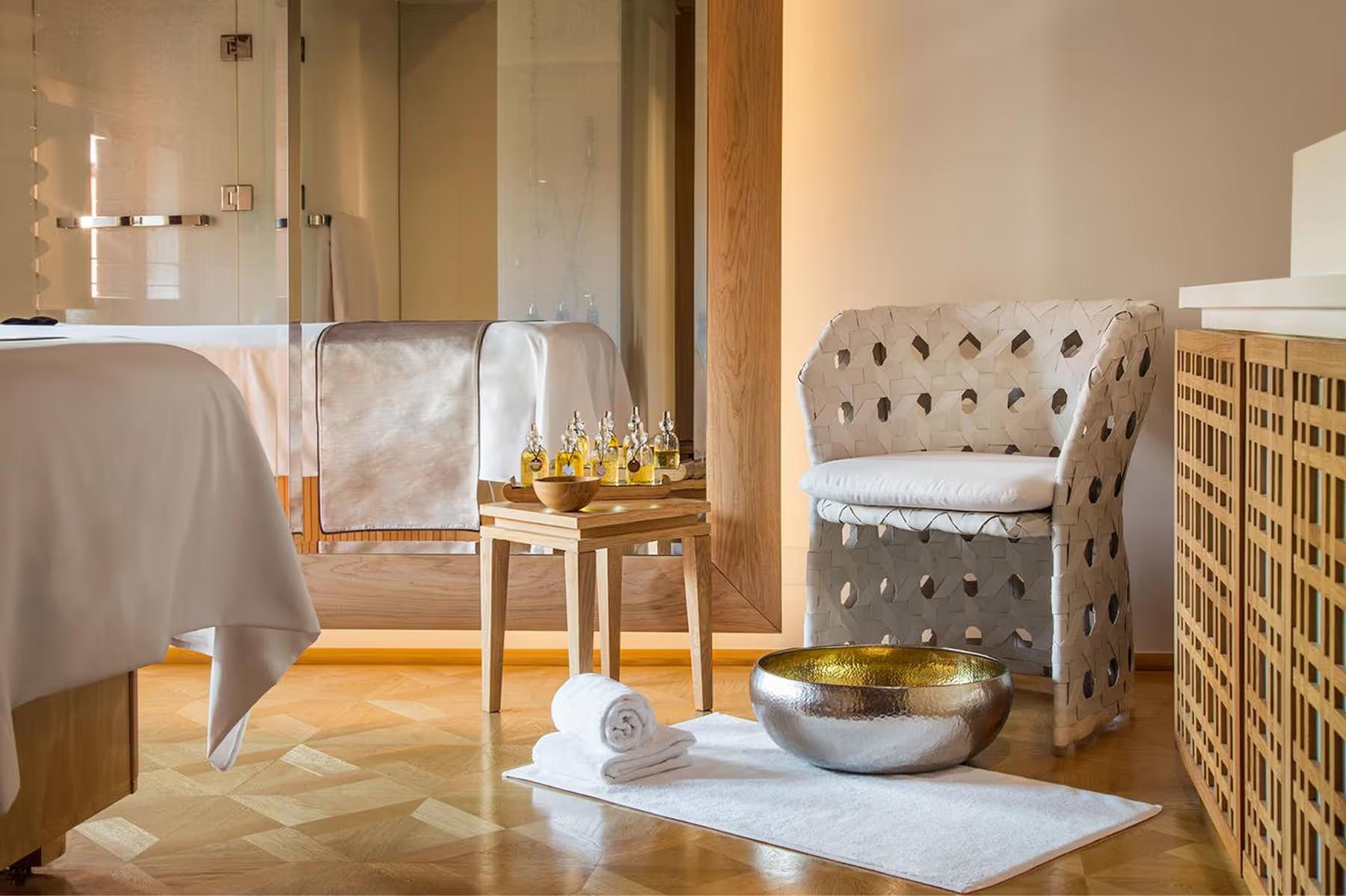 A spa treatment room with a massage table, wicker chair, natural lighting, and calm decor