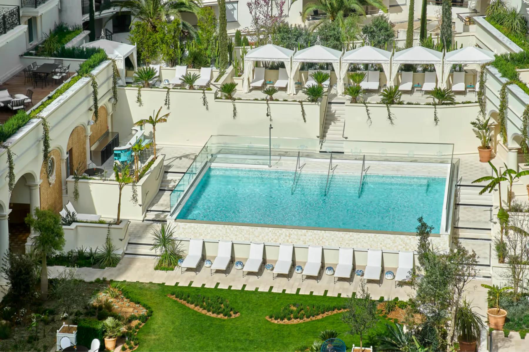 Carlton Cannes: infinity pool surrounded by white lounge beds and green lawn with hotel building in background