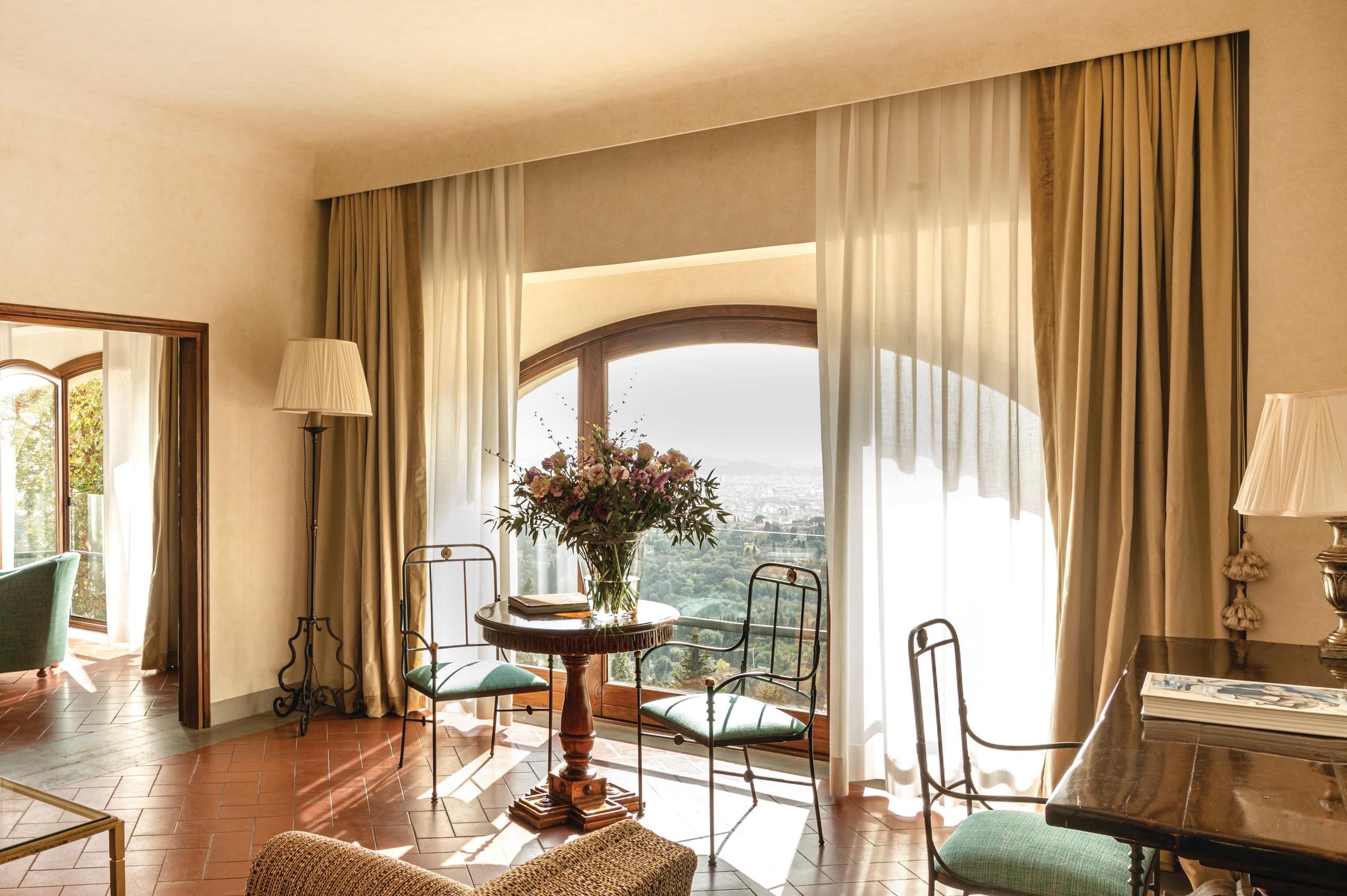 Villa San Michele: a sitting room with full-length doors, garden views, round table with flowers, and warm wood tones