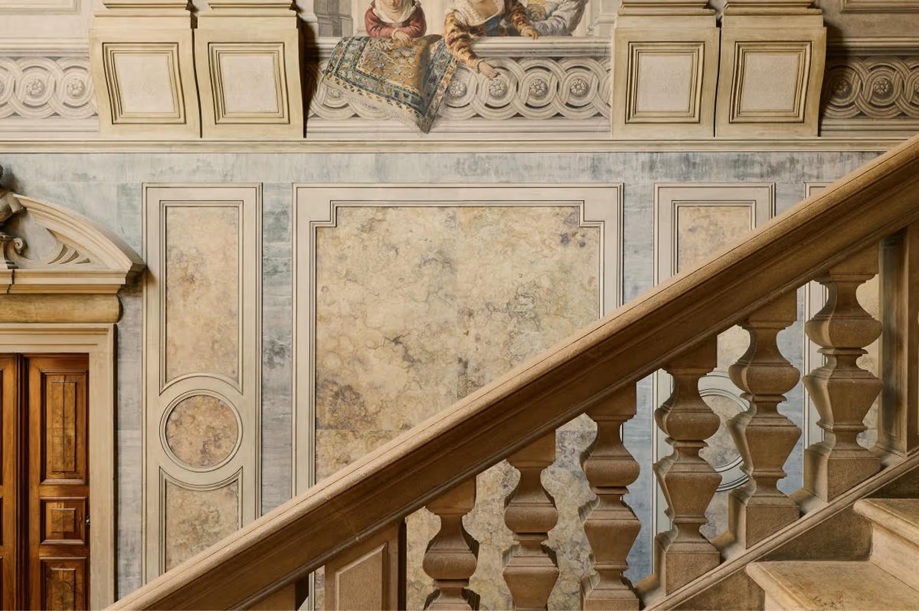 Aman Venice: a marble staircase with ornamental railings, painted ceiling with classical medallions, and cream walls