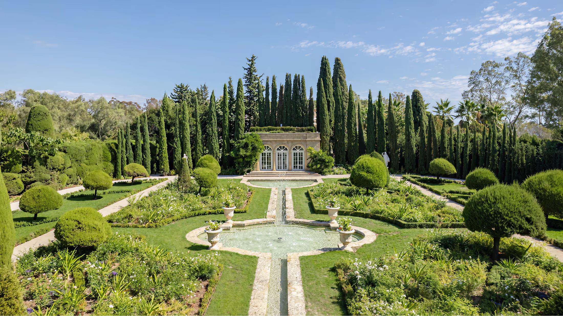 Formal gardens with manicured lawns, stone pathways, and cypress trees framing the château
