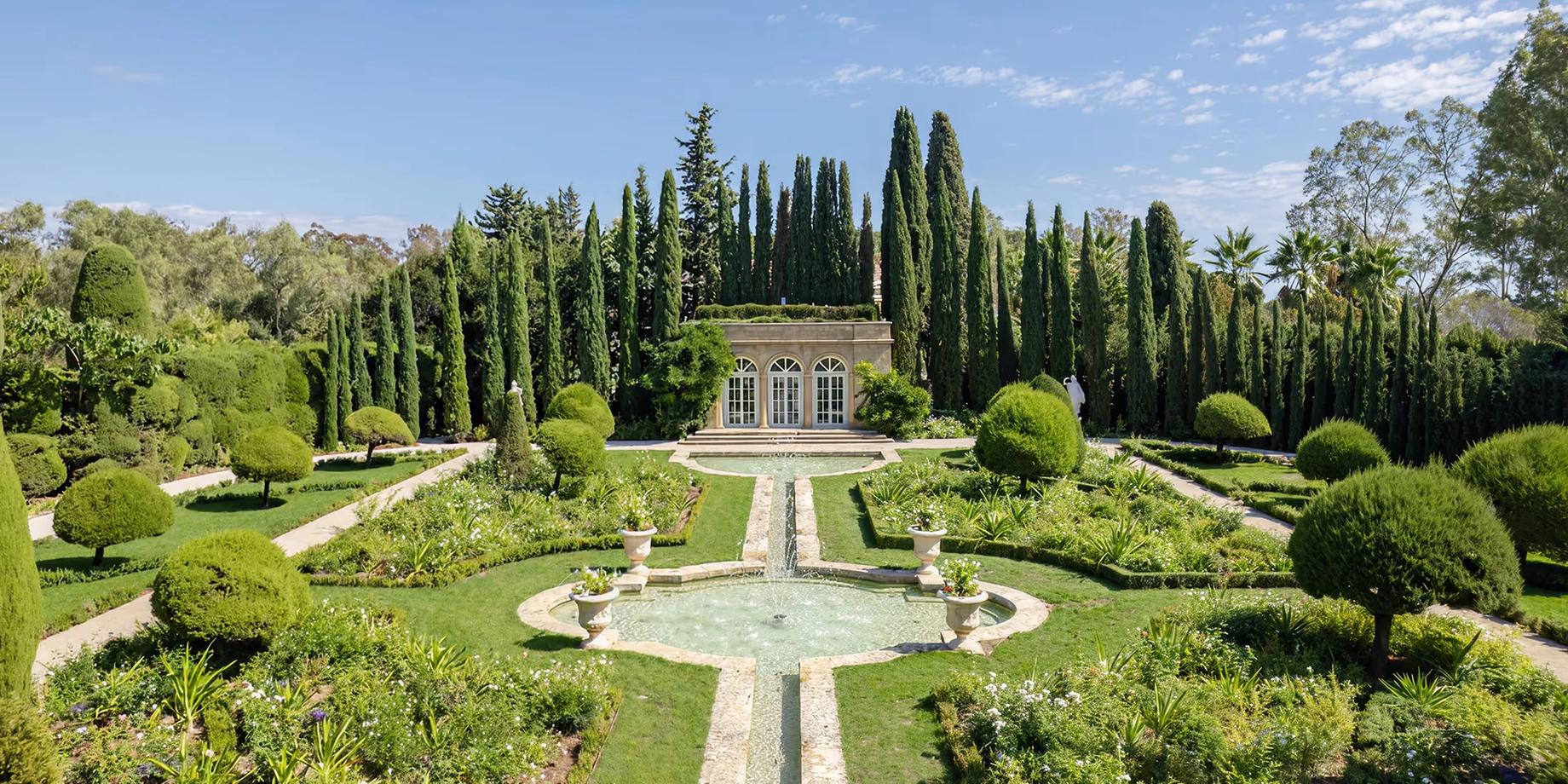 Formal gardens with manicured lawns, stone pathways, and cypress trees framing the château