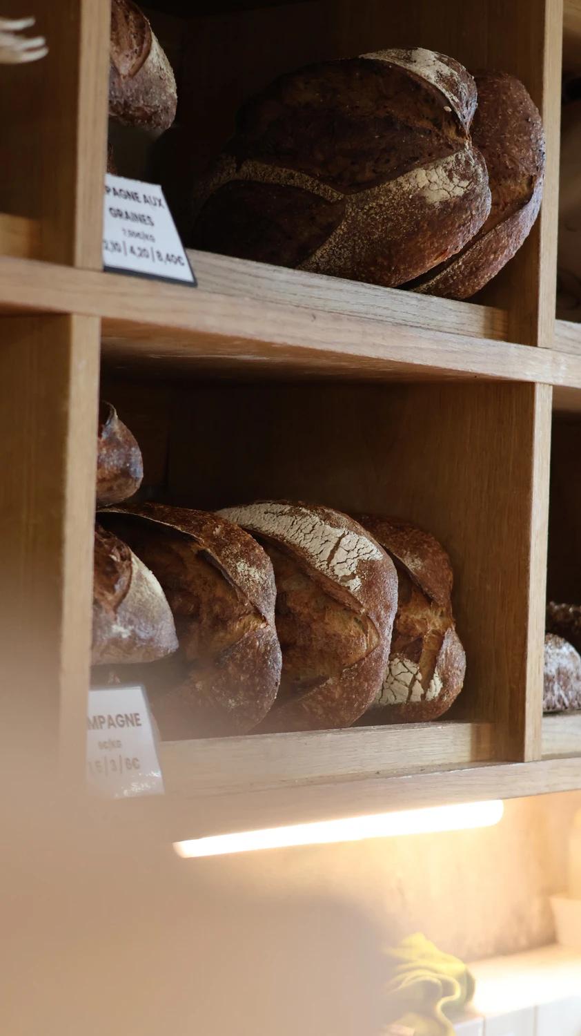 Sourdough loaves on wooden shelves with handwritten labels at Pétrin Couchette