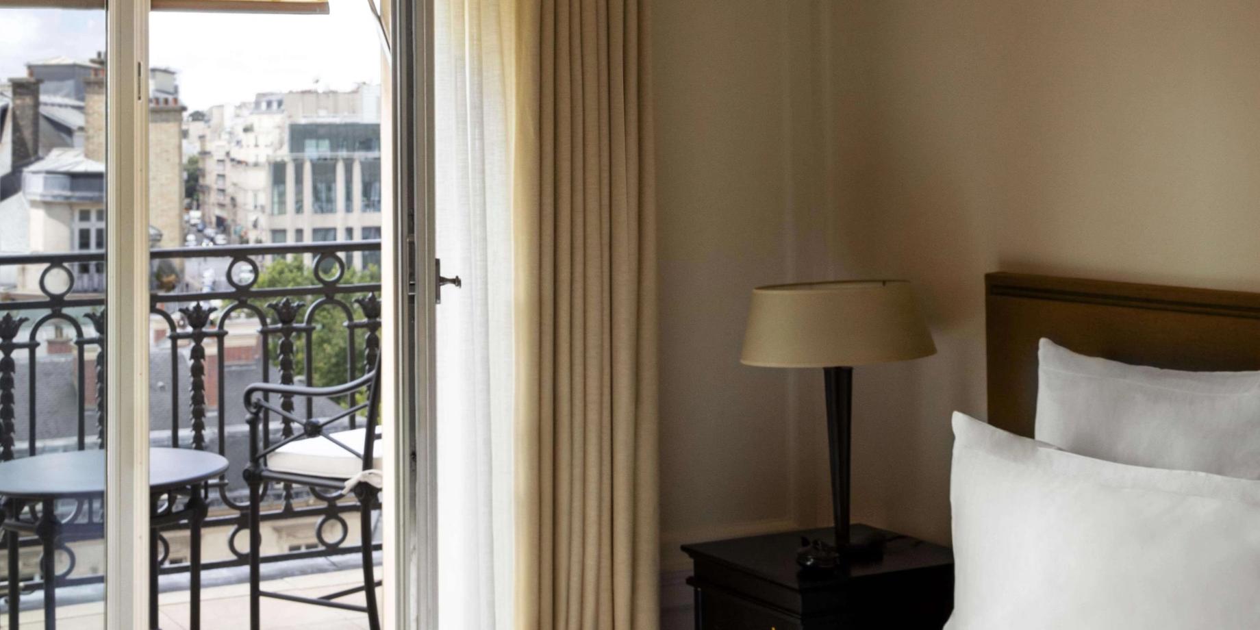 A hotel bedroom with a balcony overlooking Paris rooftops and the city