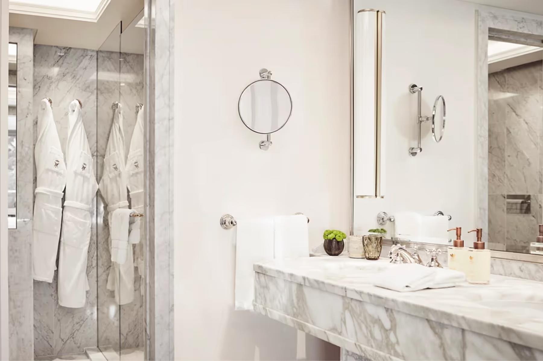 A marble bathroom with dual sinks, mirrored walls, and glass shower enclosure