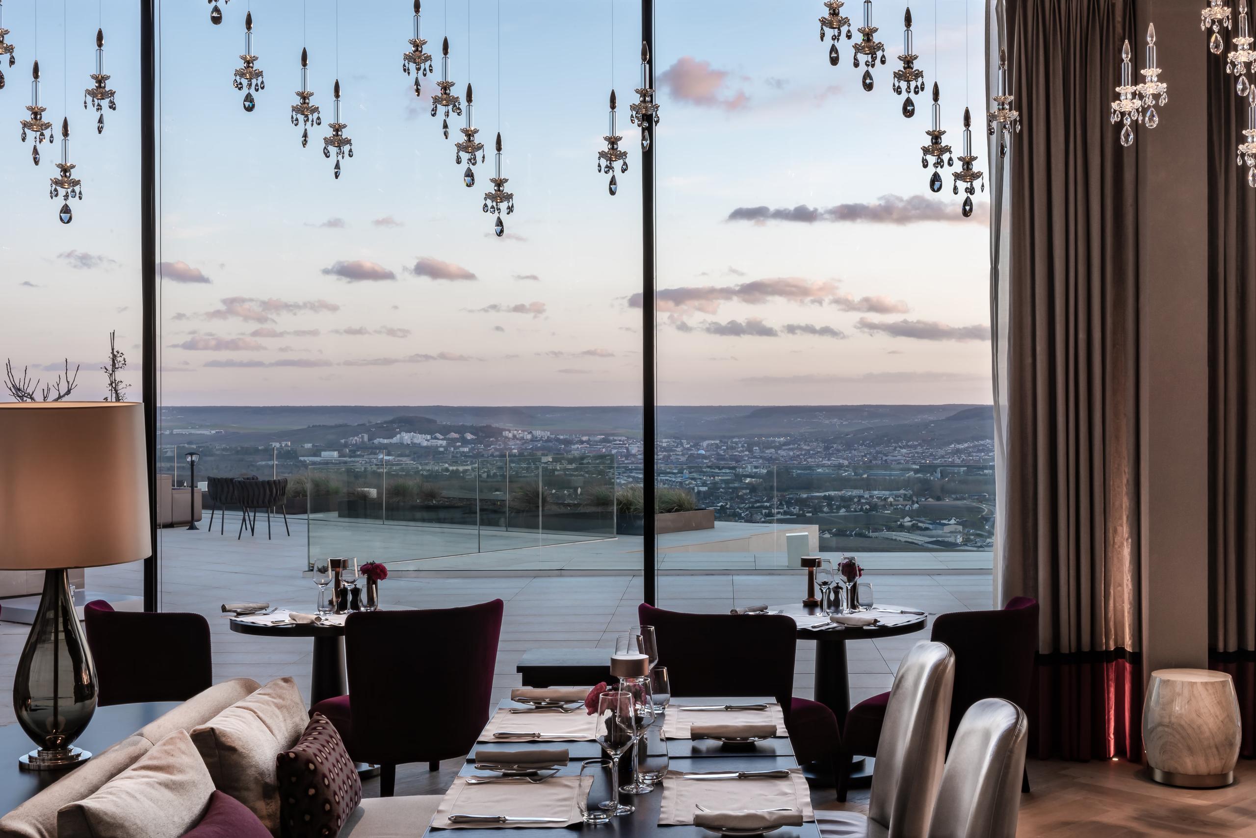 Fine dining table setting with valley landscape stretching to horizon beyond floor-to-ceiling windows