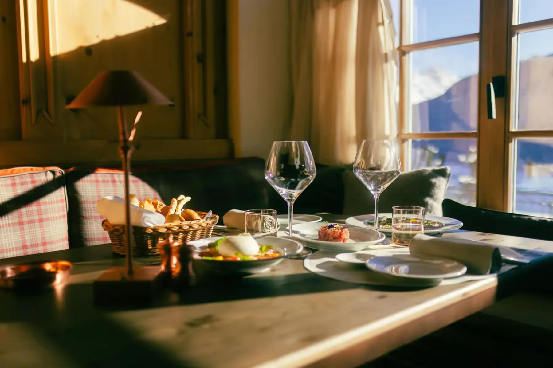 A fine dining table set with wine glasses and white linens beside snowy windows