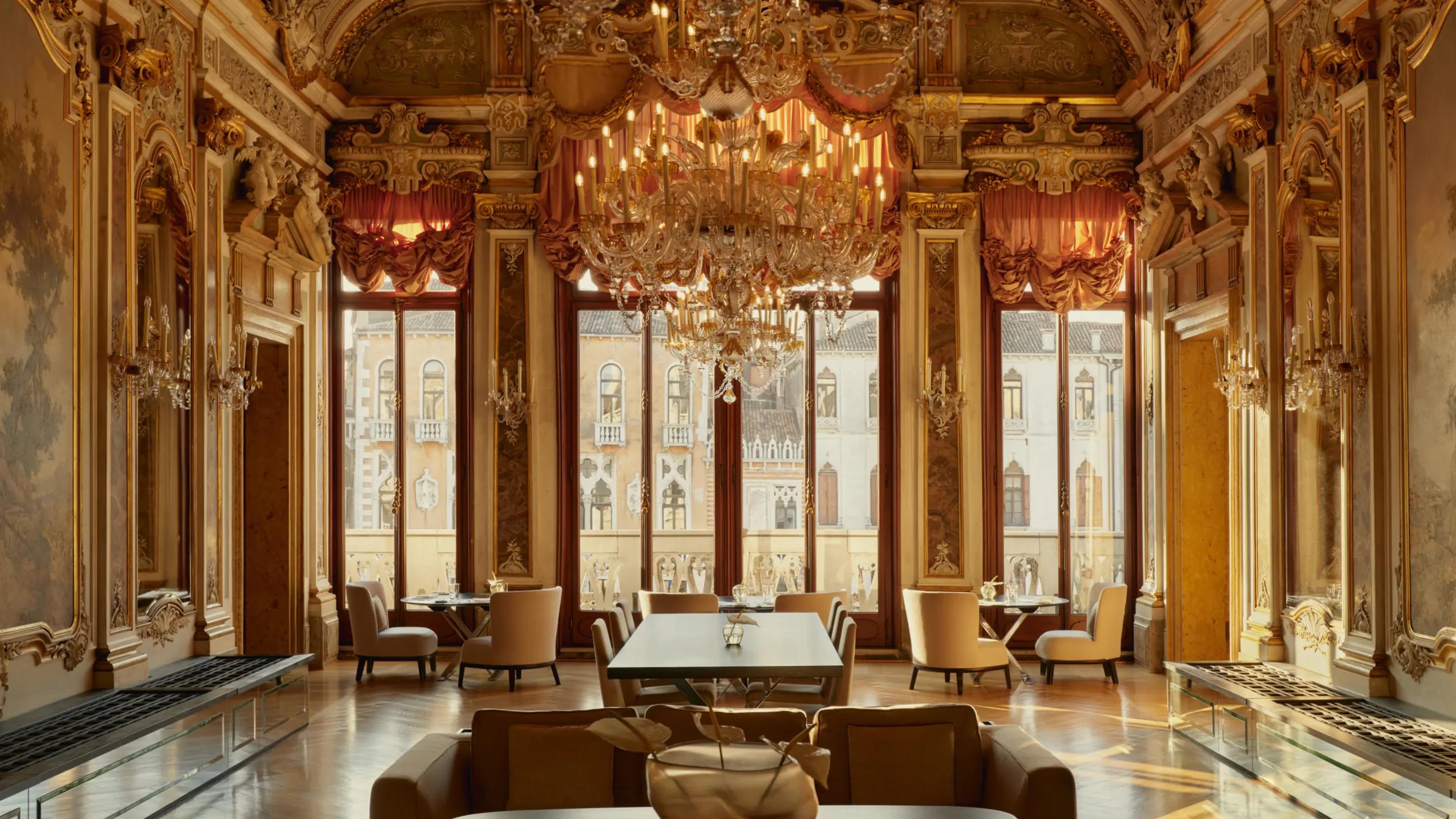 A grand gilded Venetian salon with a large crystal chandelier and tall arched windows over the Grand Canal