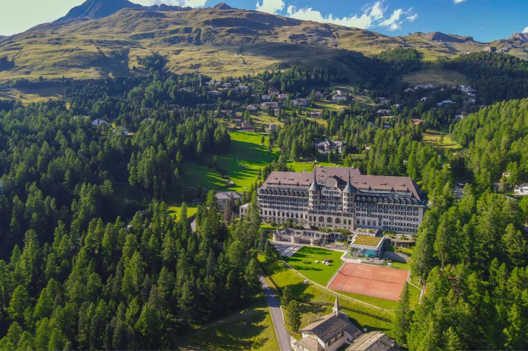 The hotel with surrounding forest and mountains, viewed from a distant elevated vantage point