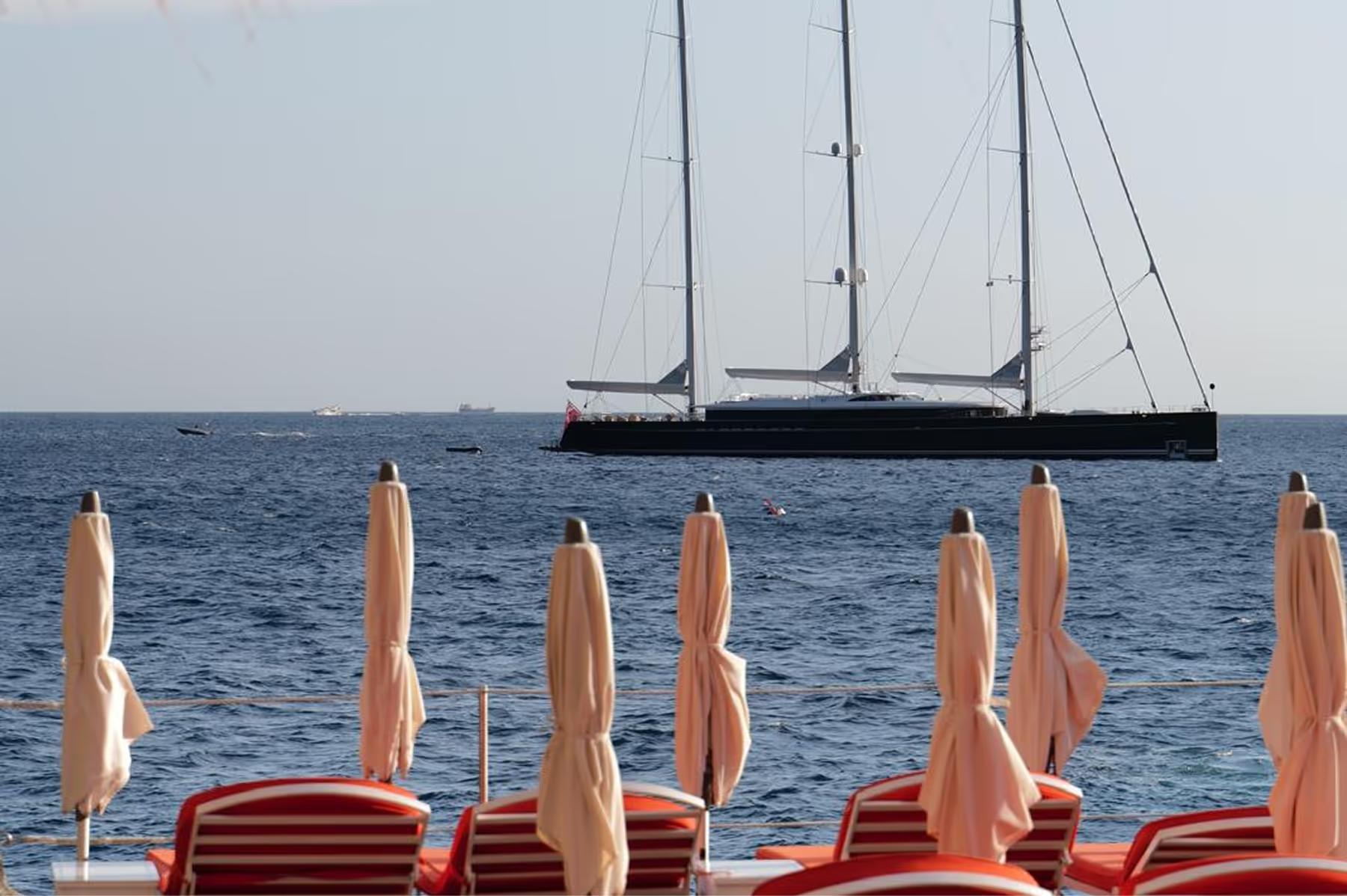 Luxury sailing yacht on blue water with striped umbrellas and lounges in foreground