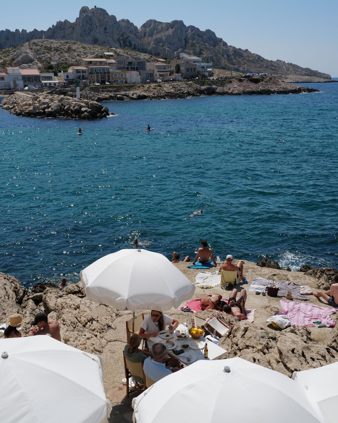 Swimmers and white parasols on the rocks above the sea in Marseille