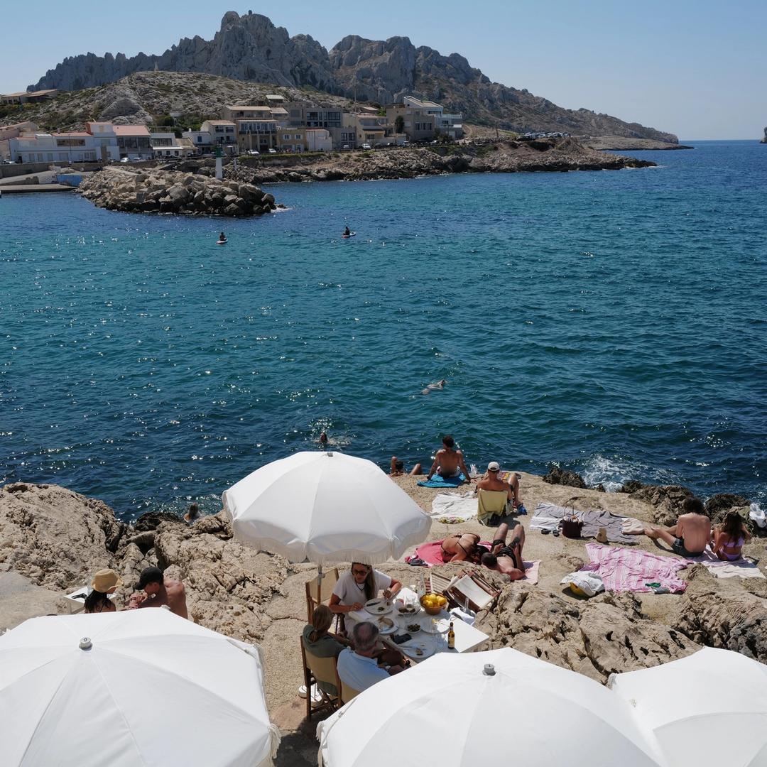 Swimmers and white parasols on the rocks above the sea in Marseille