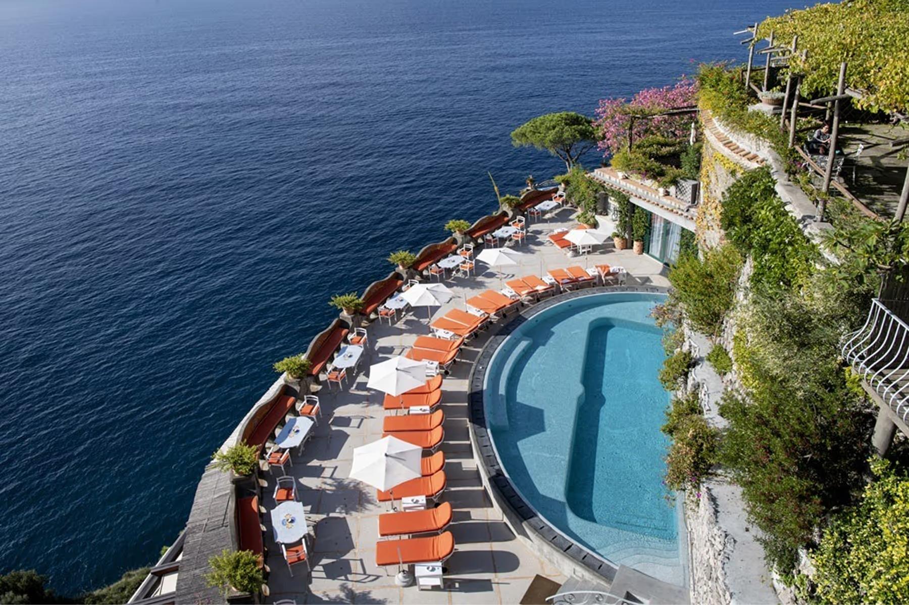 Elevated view of pool deck with striped orange lounges, blue water, and surrounding coastal landscape