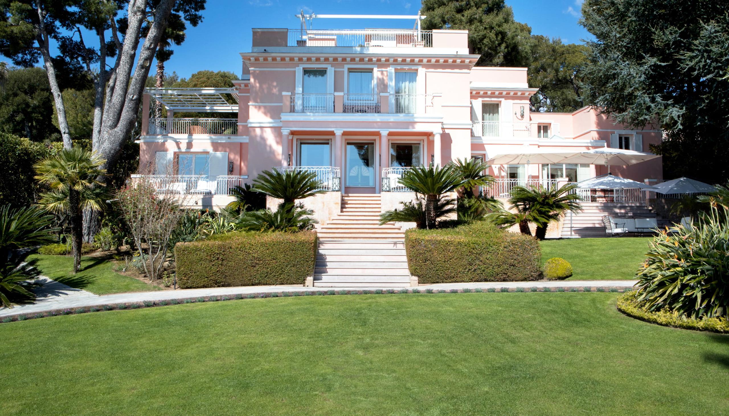 Pink and blue villa with manicured gardens and palm trees
