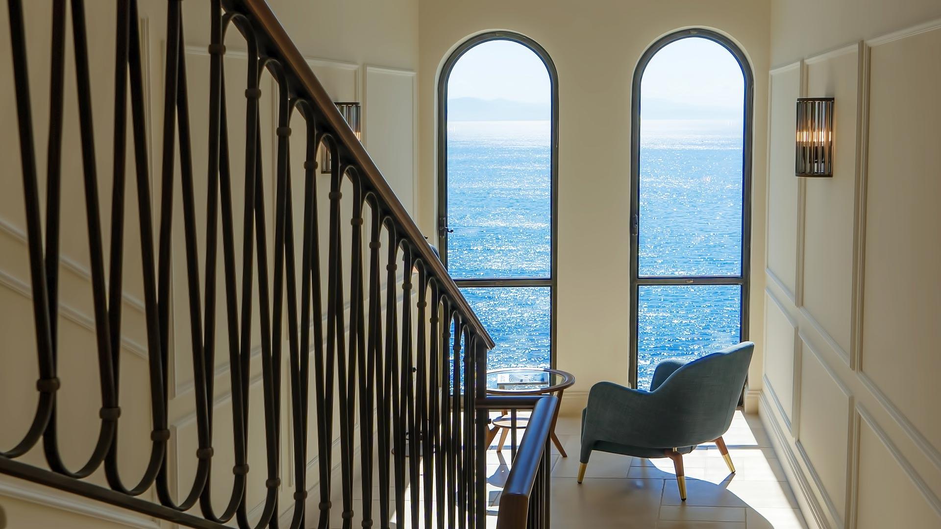 Borgo Santandrea: stairwell with black railings framing arched windows overlooking the sea