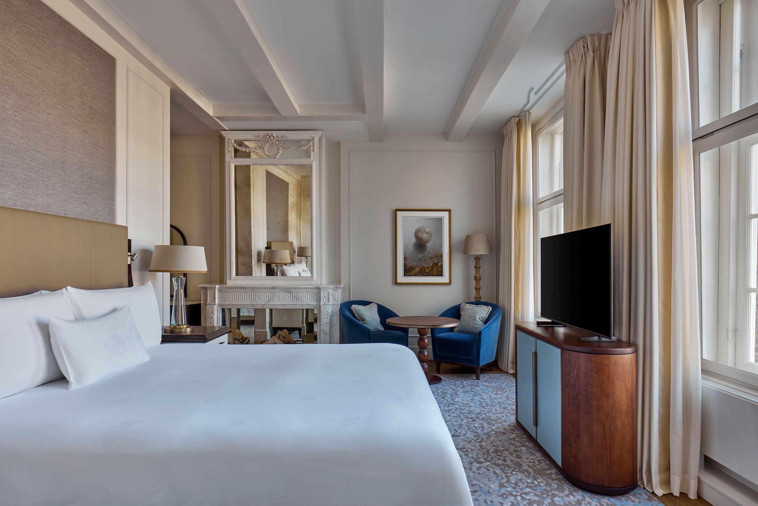 Waldorf Astoria Amsterdam: a guest room with a cream headboard, white bedding, blue accent chairs, and tall windows with draped curtains