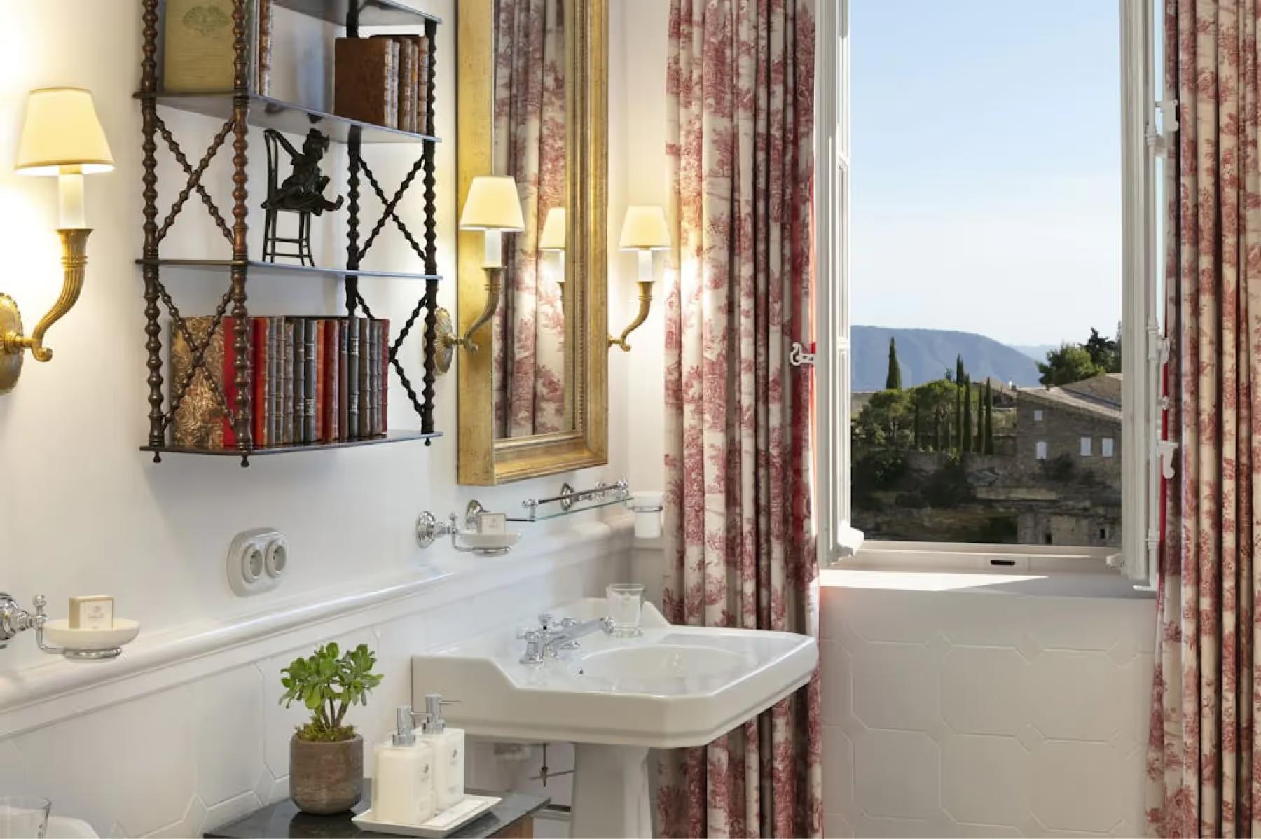 Airelles Gordes, La Bastide: bathroom with porthole mirror and shower door overlooking mountains