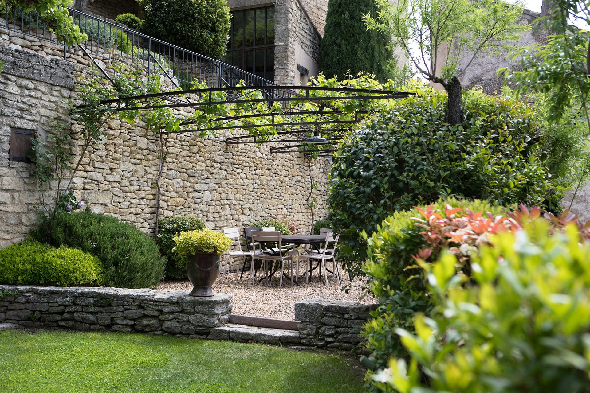 Airelles Gordes, La Bastide: garden terrace with stone walls, flowering plants, and metal furniture