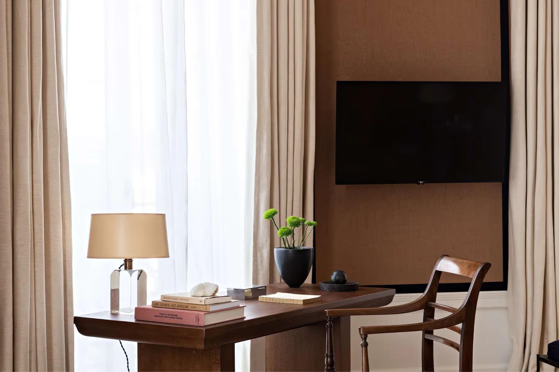 A desk and chair in a room with tan and brown tones and large windows
