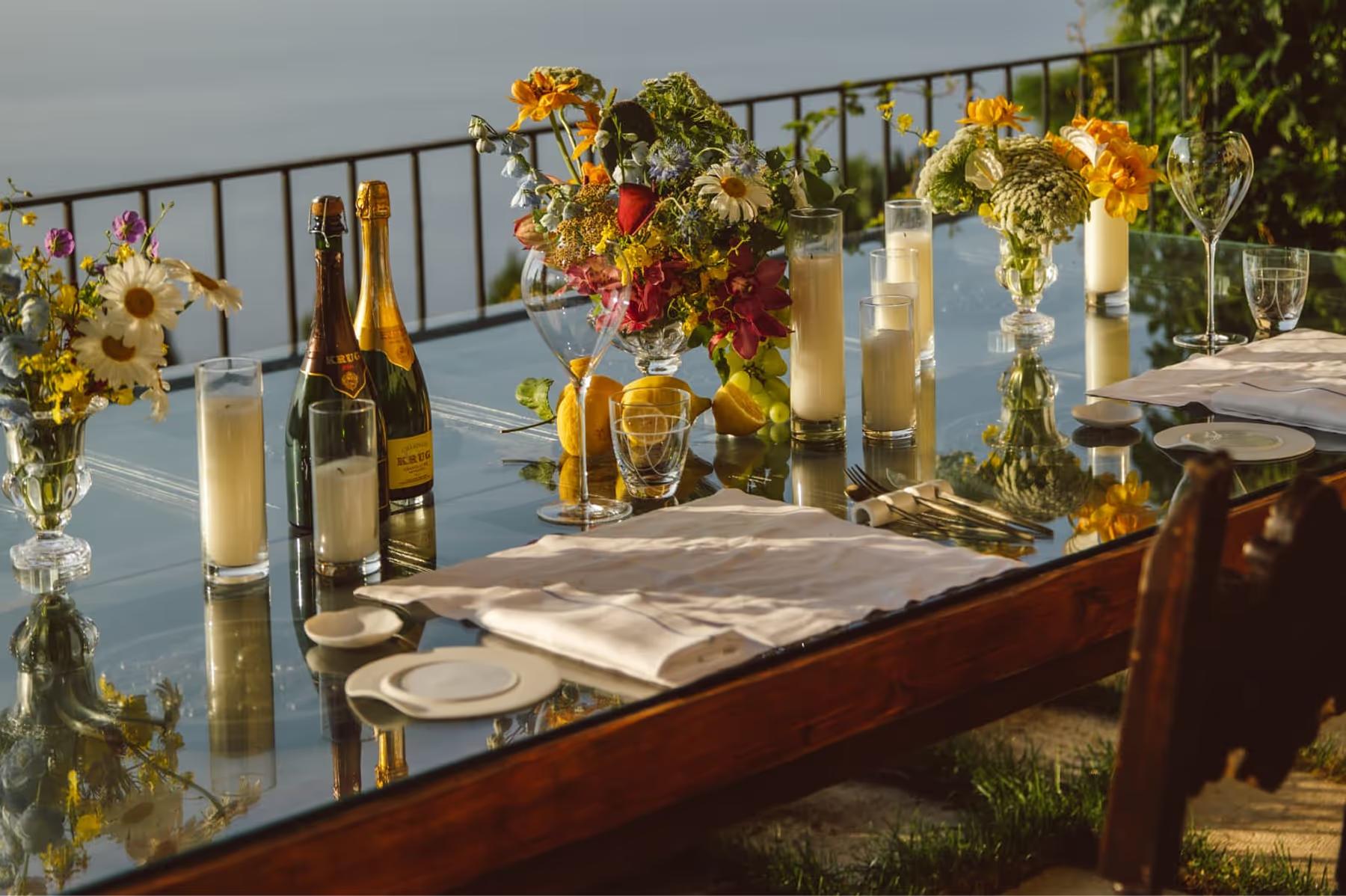Caruso: cliffside table setting with floral arrangements, golden wine glasses, sea vista and mountains beyond