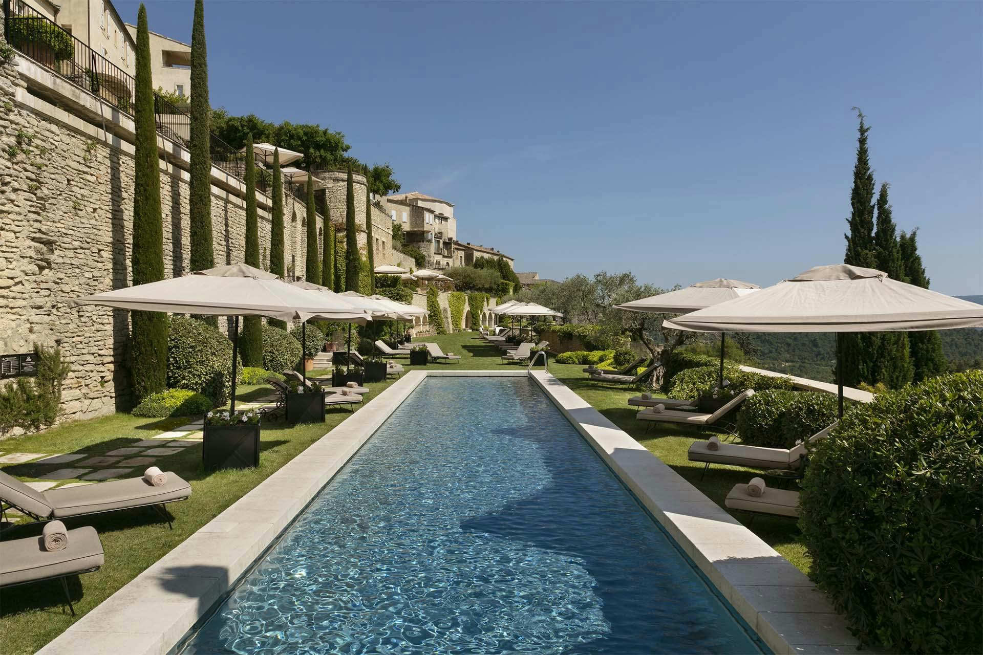 Airelles Gordes, La Bastide: rectangular pool with loungers and white umbrellas framed by stone columns