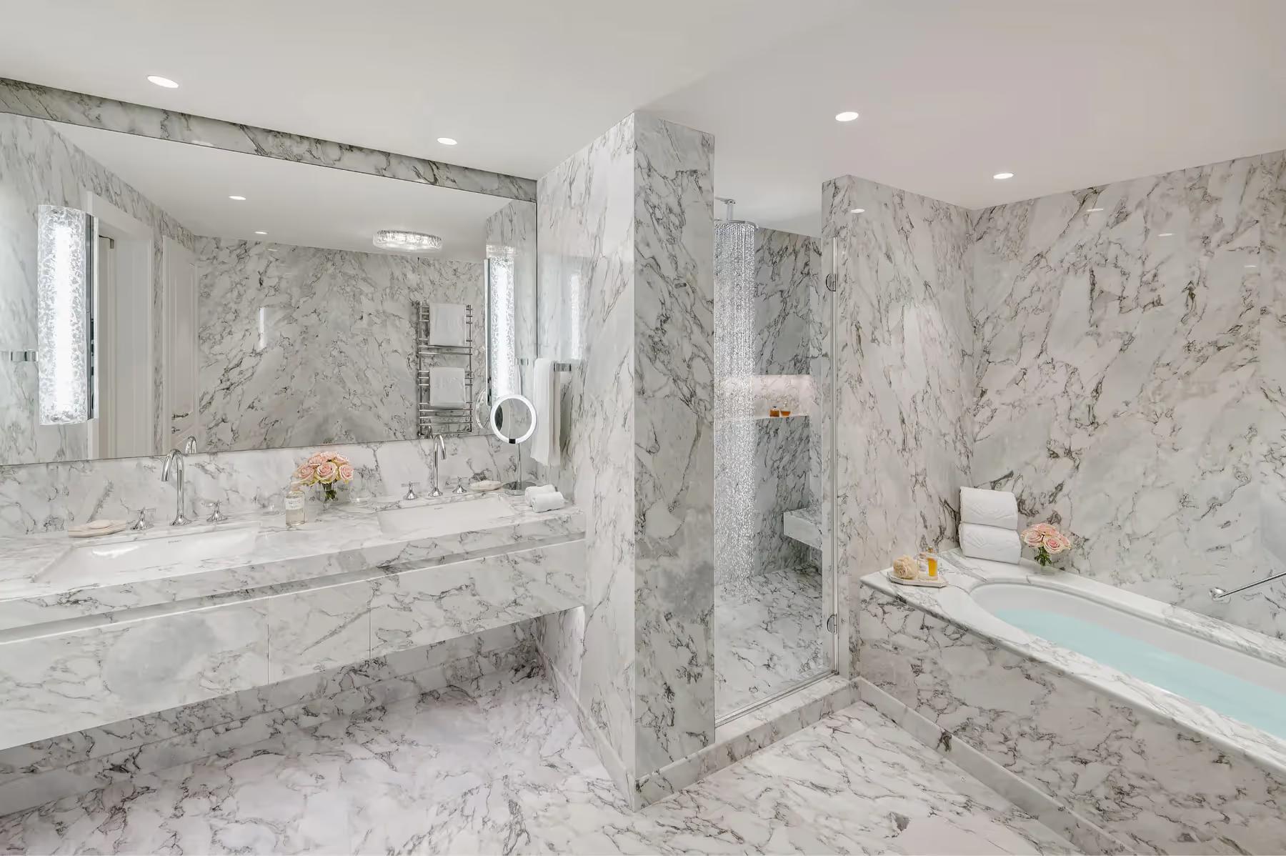 Modern bathroom with marble surfaces, walk-in shower, and dual vanities