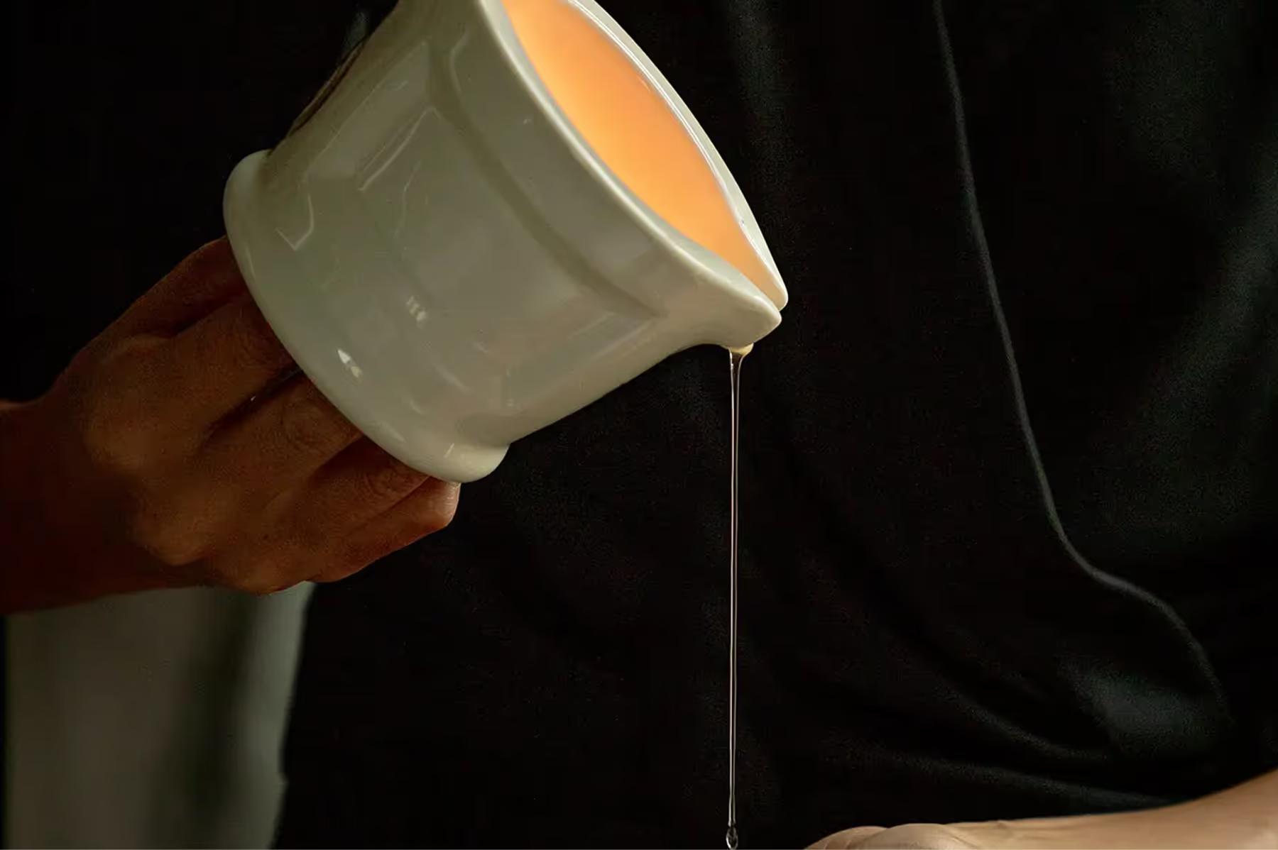 Hands pouring ritualistic hammam oil into ceramic bowl