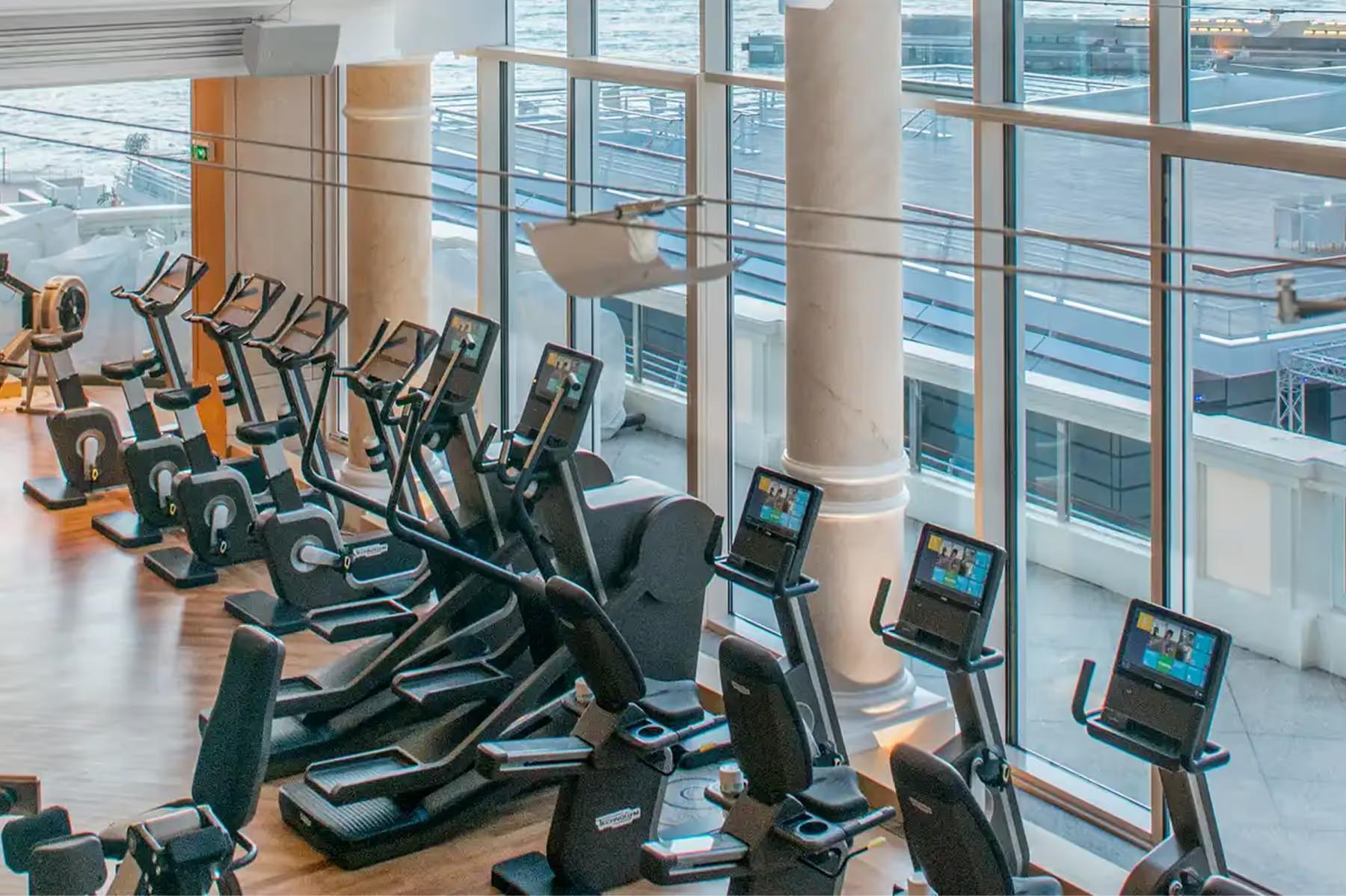 Fitness studio with stationary bikes facing floor-to-ceiling windows over water