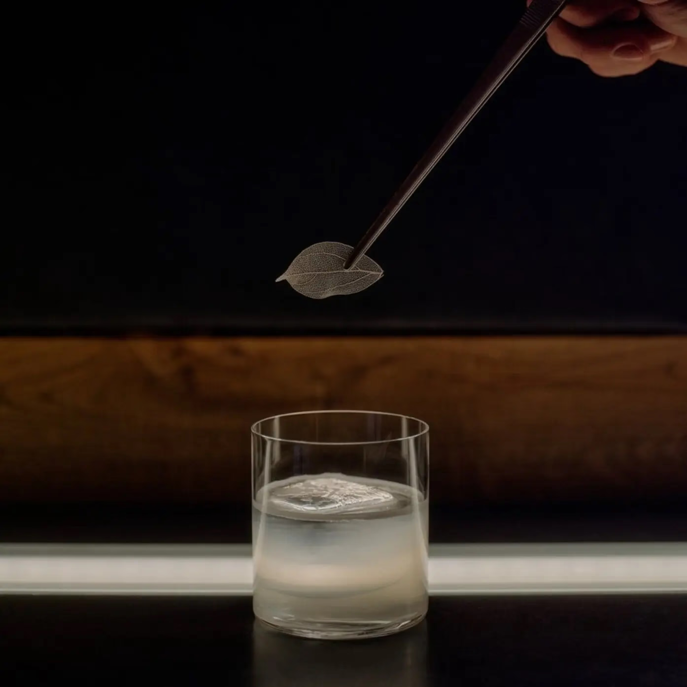 Cocktail garnished with a dried leaf, poured tableside over ice in a low rocks glass