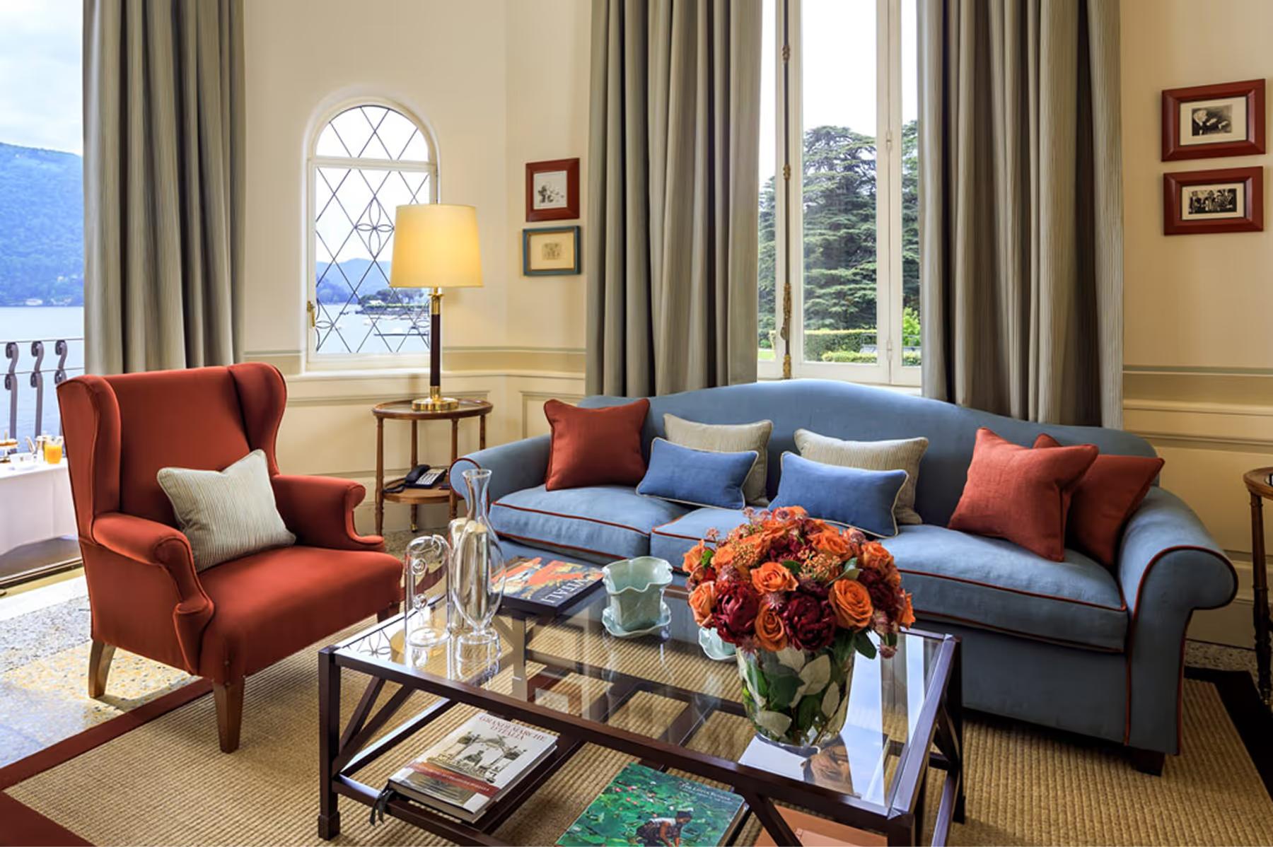 Villa d’Este: sitting area with red armchair, decorative pillows, framed artwork, and large windows