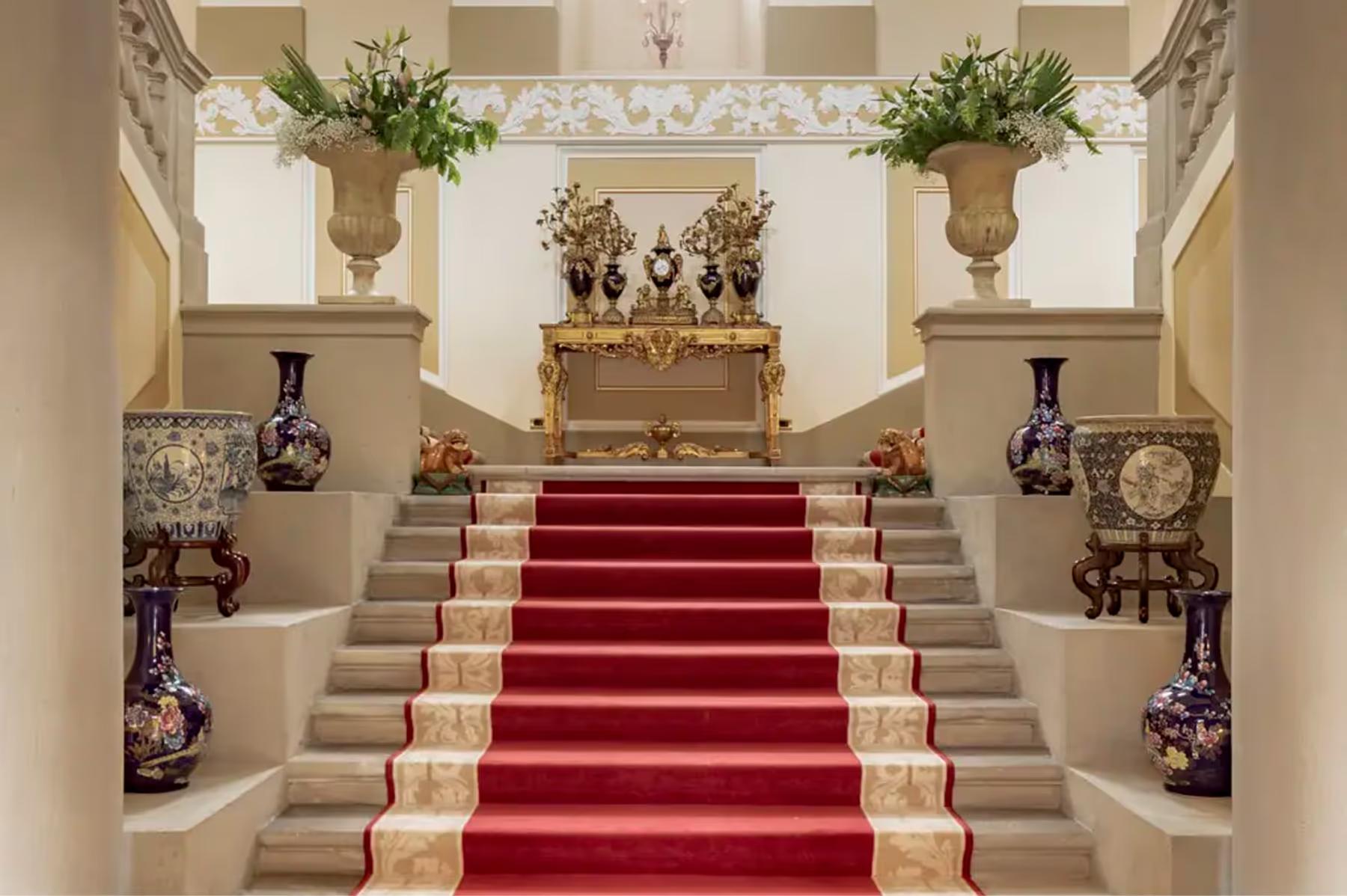 A grand staircase with marble treads, green carpet runner, and ornate balustrades