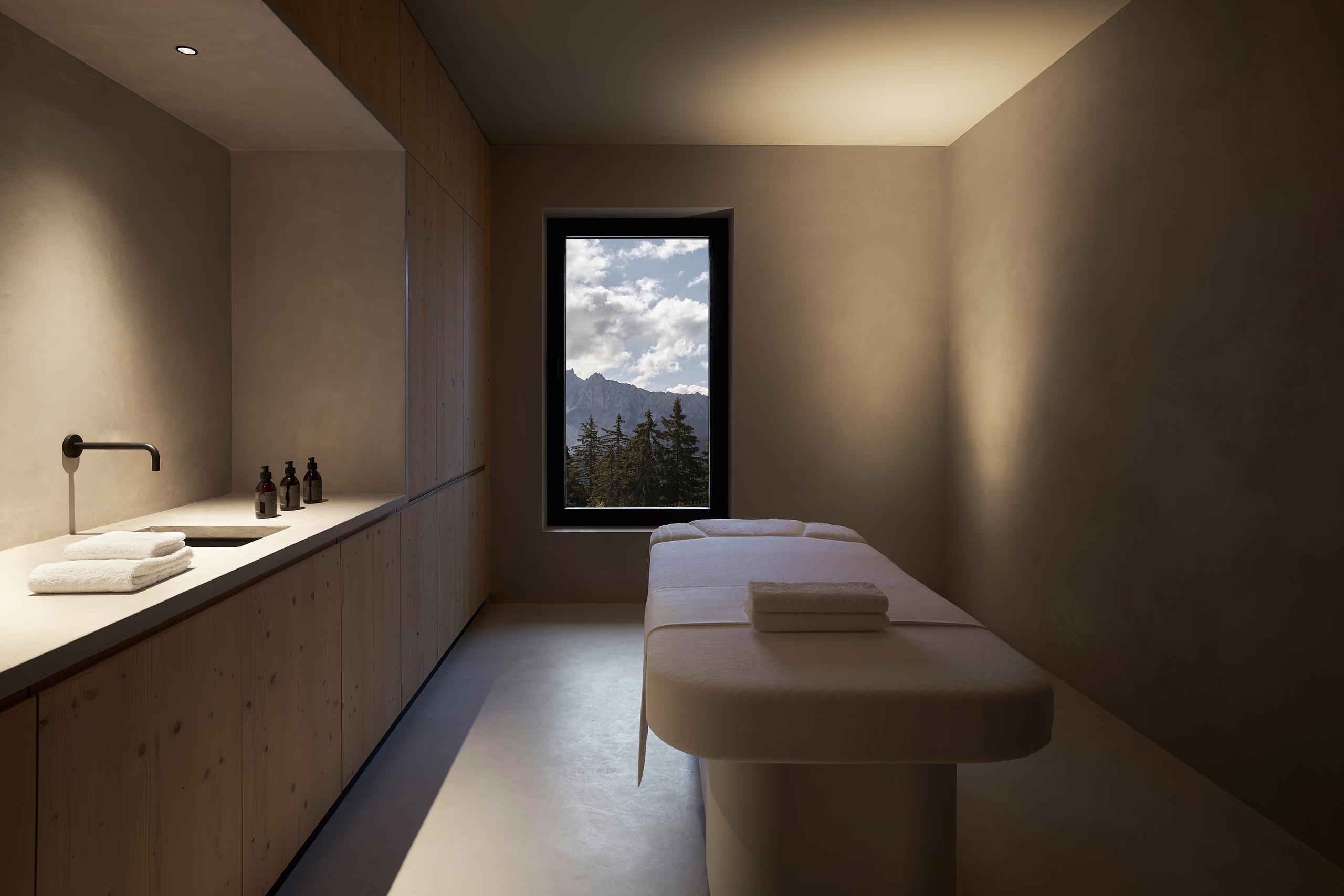 A massage or treatment room with light wood finishes, a treatment bench, and a framed window view
