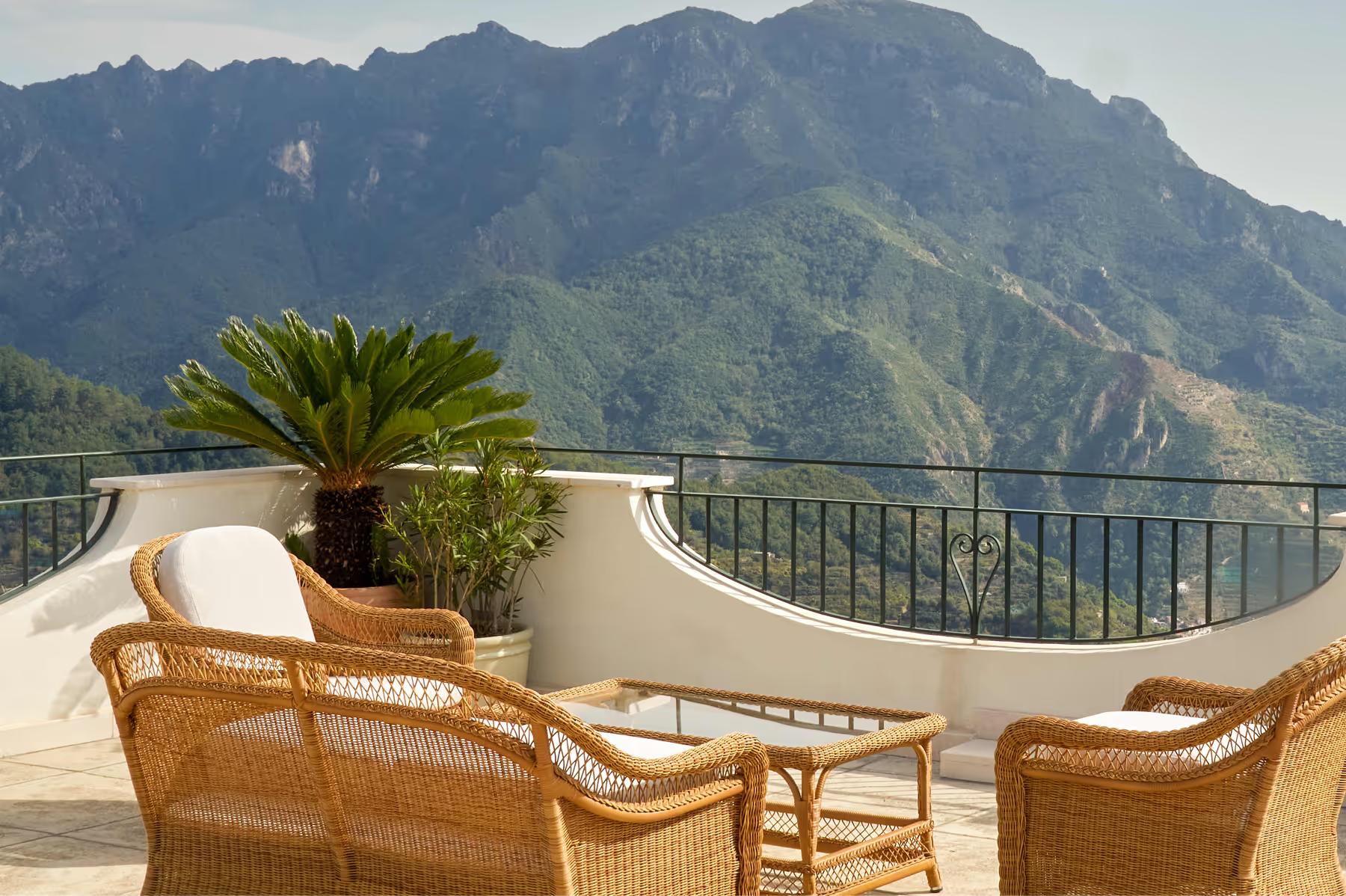 Caruso: terrace with wicker chairs, palm plants, turquoise Mediterranean vista and distant mountains at dusk