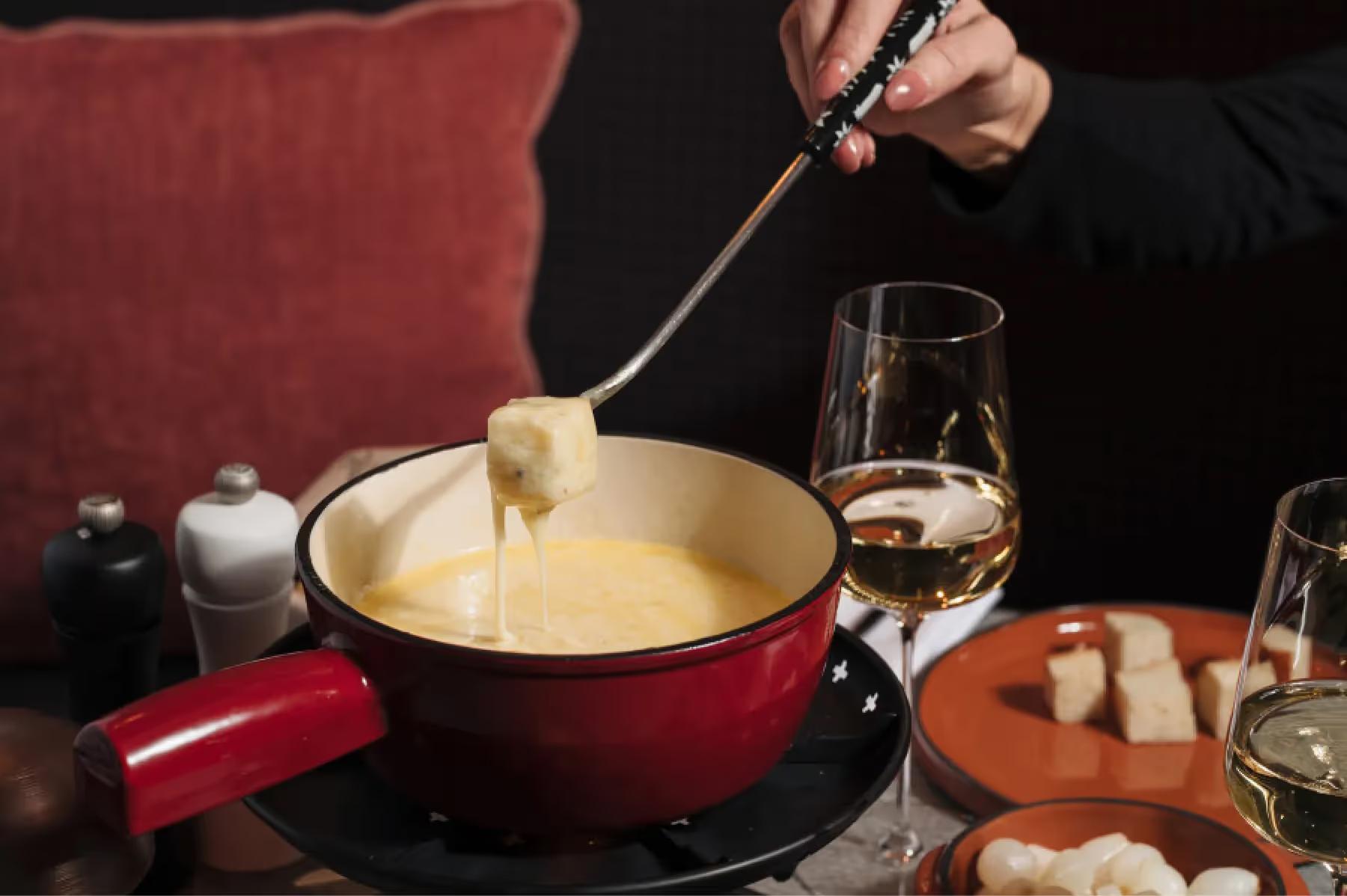 Fondue pot with melted cheese being stirred with fork over table service items