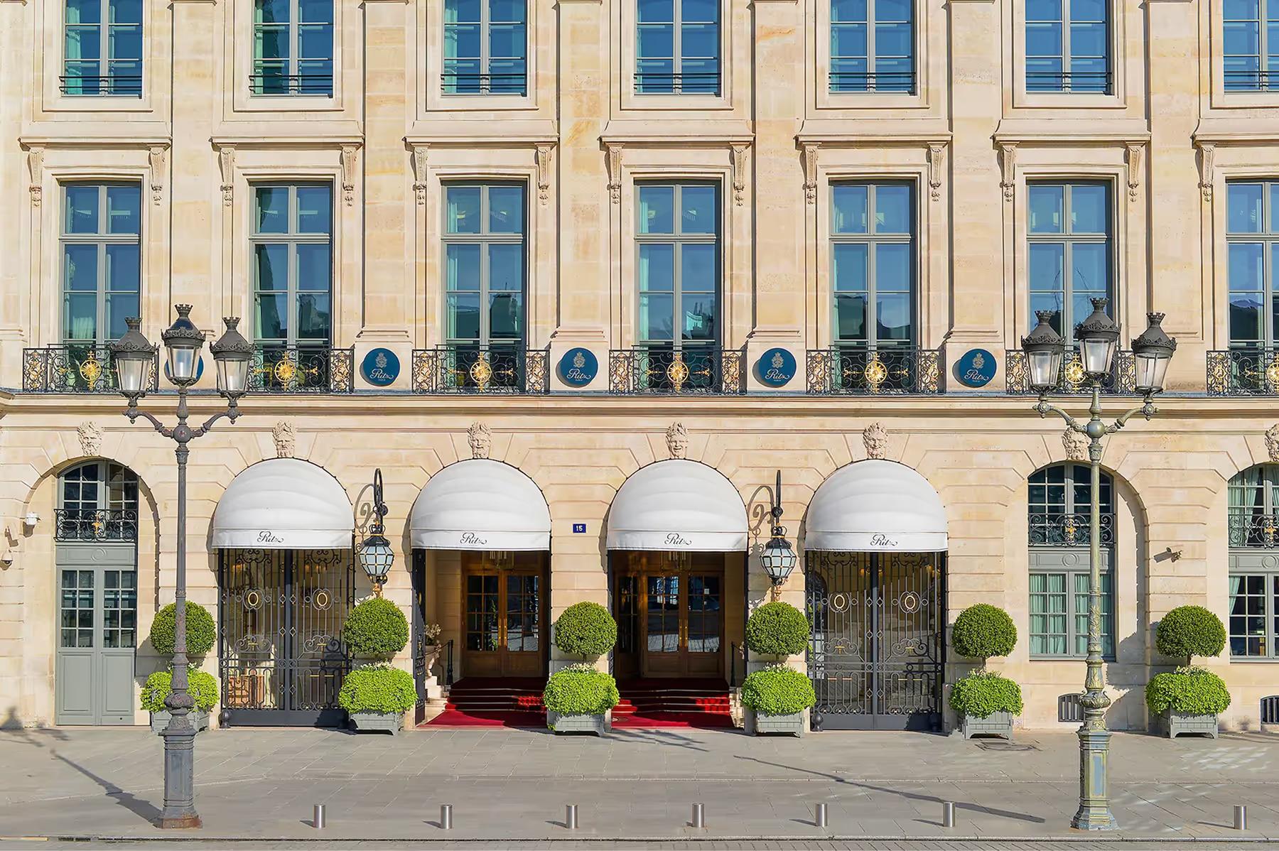 The Ritz Paris facade on Place Vendôme with golden stone, arched entrances, and topiary-lined forecourt