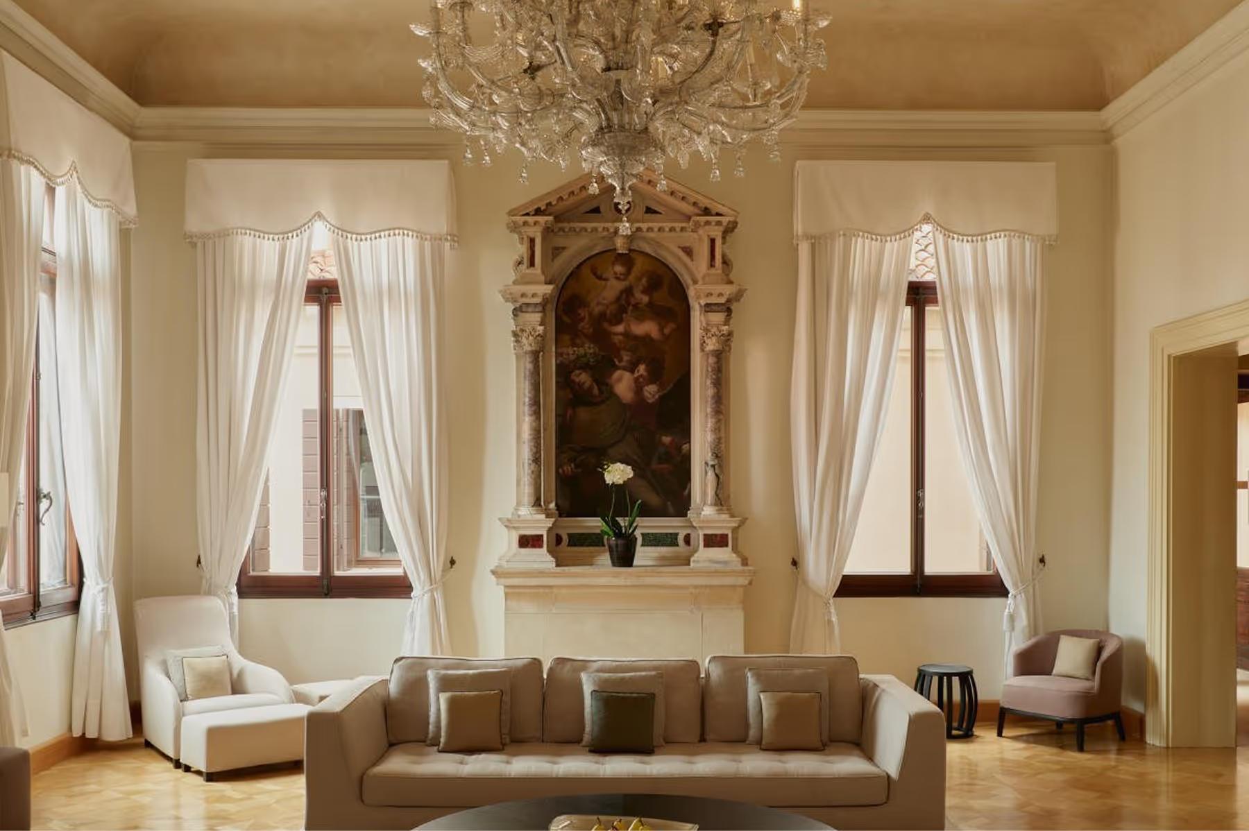 A neoclassical sitting room with symmetrical arched niches, white painted panels, cream upholstered seating, and a crystal chandelier