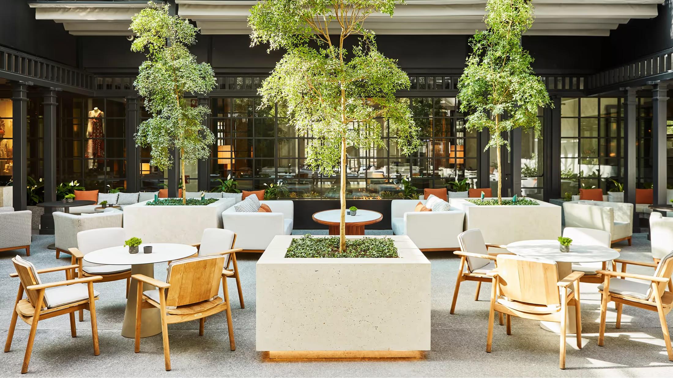 The hotel courtyard with lush trees, white seating, and columned architecture in Madrid